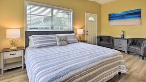 A bedroom with a large bed, two bedside tables, a ceiling fan, a door, and a painting on the wall. - 'sarasota Sunset House' w/ Spacious Patio! (Sarasota)