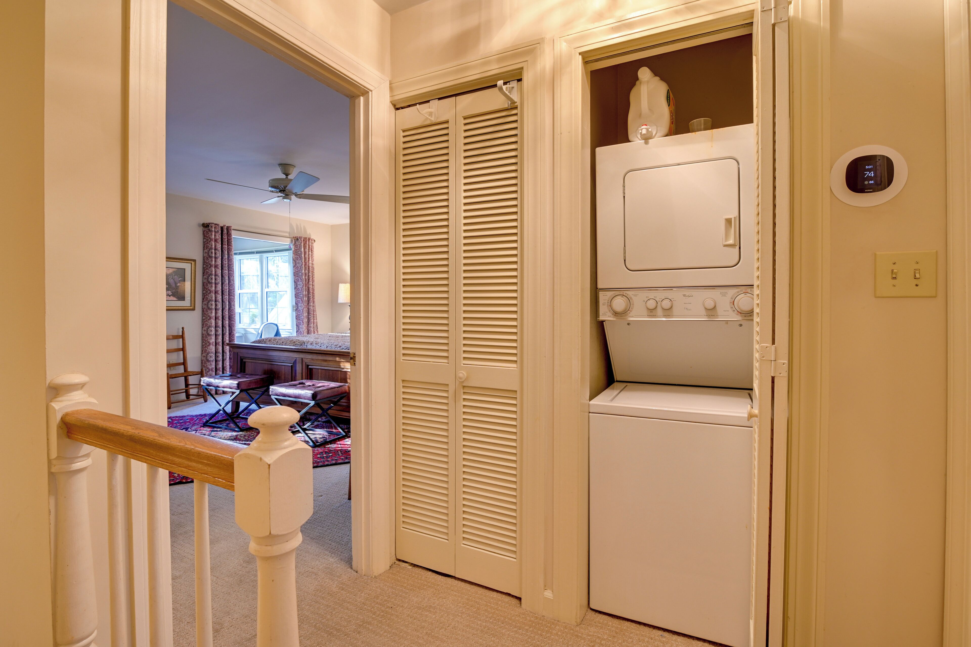 A laundry room with a washing machine and dryer, a ceiling fan, and a thermostat on the wall.