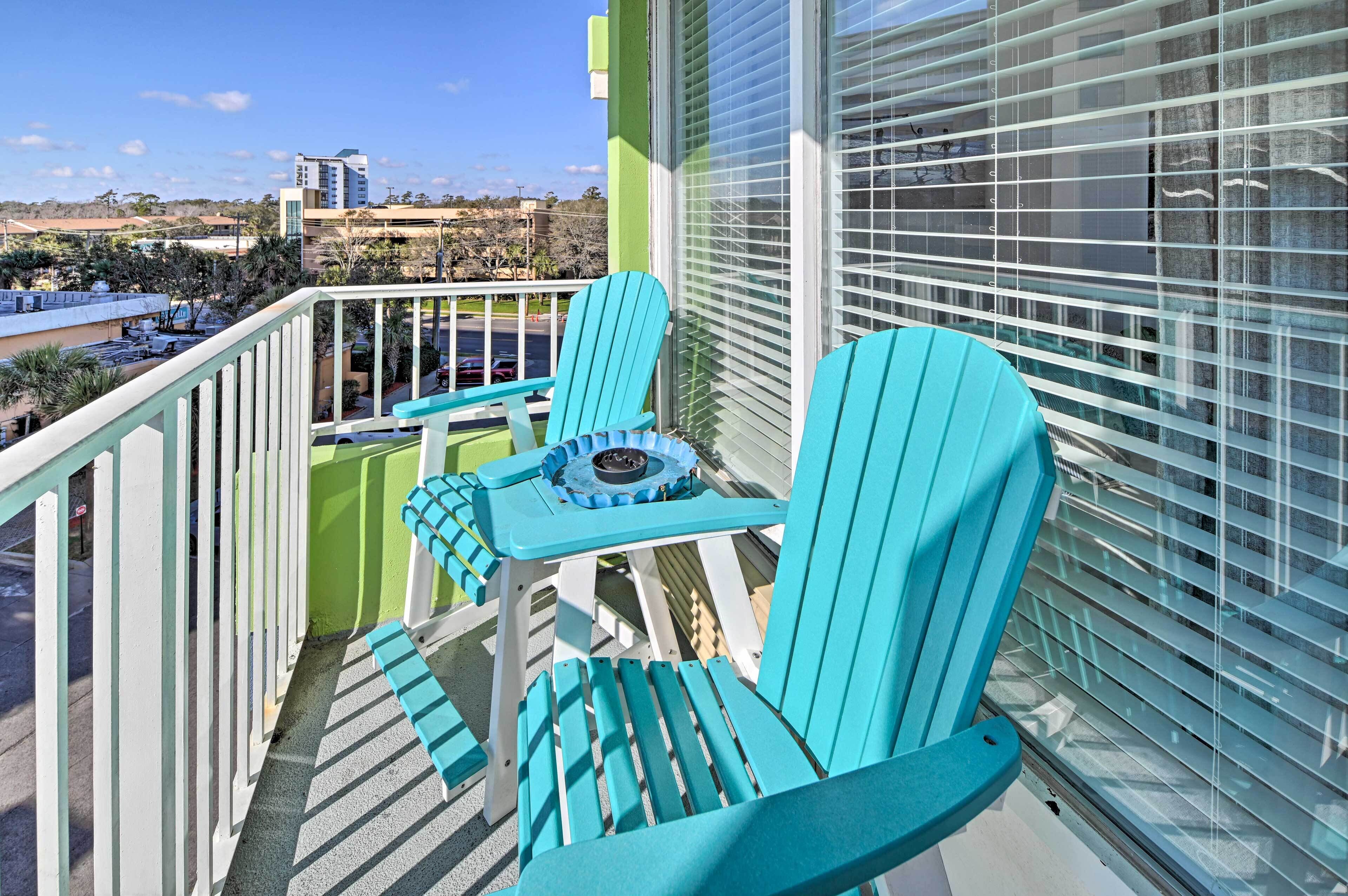 Een balkon met turquoise stoelen en een tafeltje, met uitzicht op een stadsgezicht.
