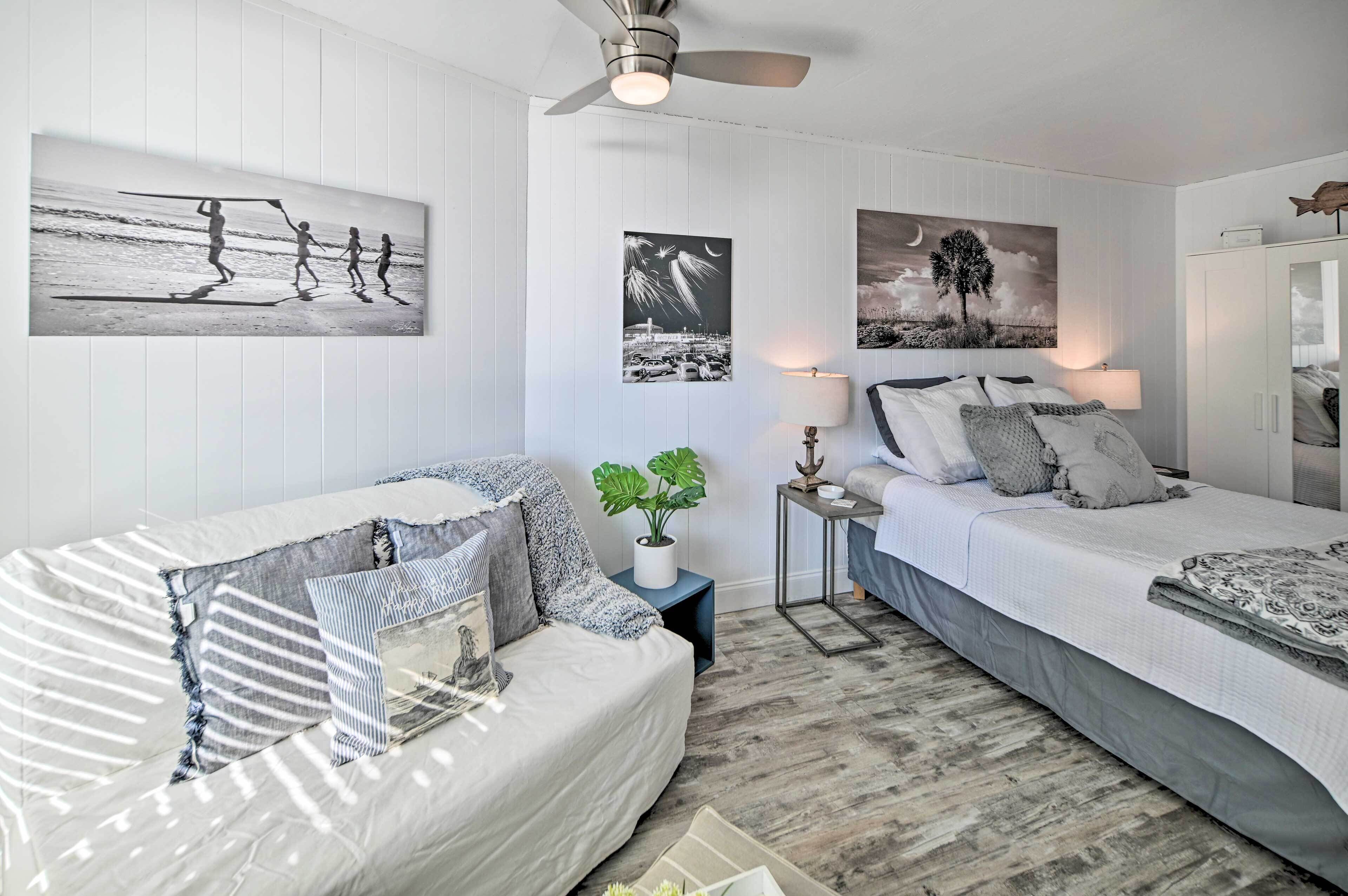A bedroom with two beds, a ceiling fan, and wall art depicting beach scenes and a tree.