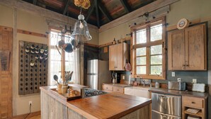 A rustic kitchen with wooden cabinets, a central island, stainless steel appliances, and a hanging light fixture. - Views & Trails: Horse Farm Home in Campobello! (Campobello)