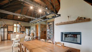 A spacious dining area with a wooden table and chairs, a kitchen in the background, and a fireplace with a metal screen. - Views & Trails: Horse Farm Home in Campobello! (Campobello)