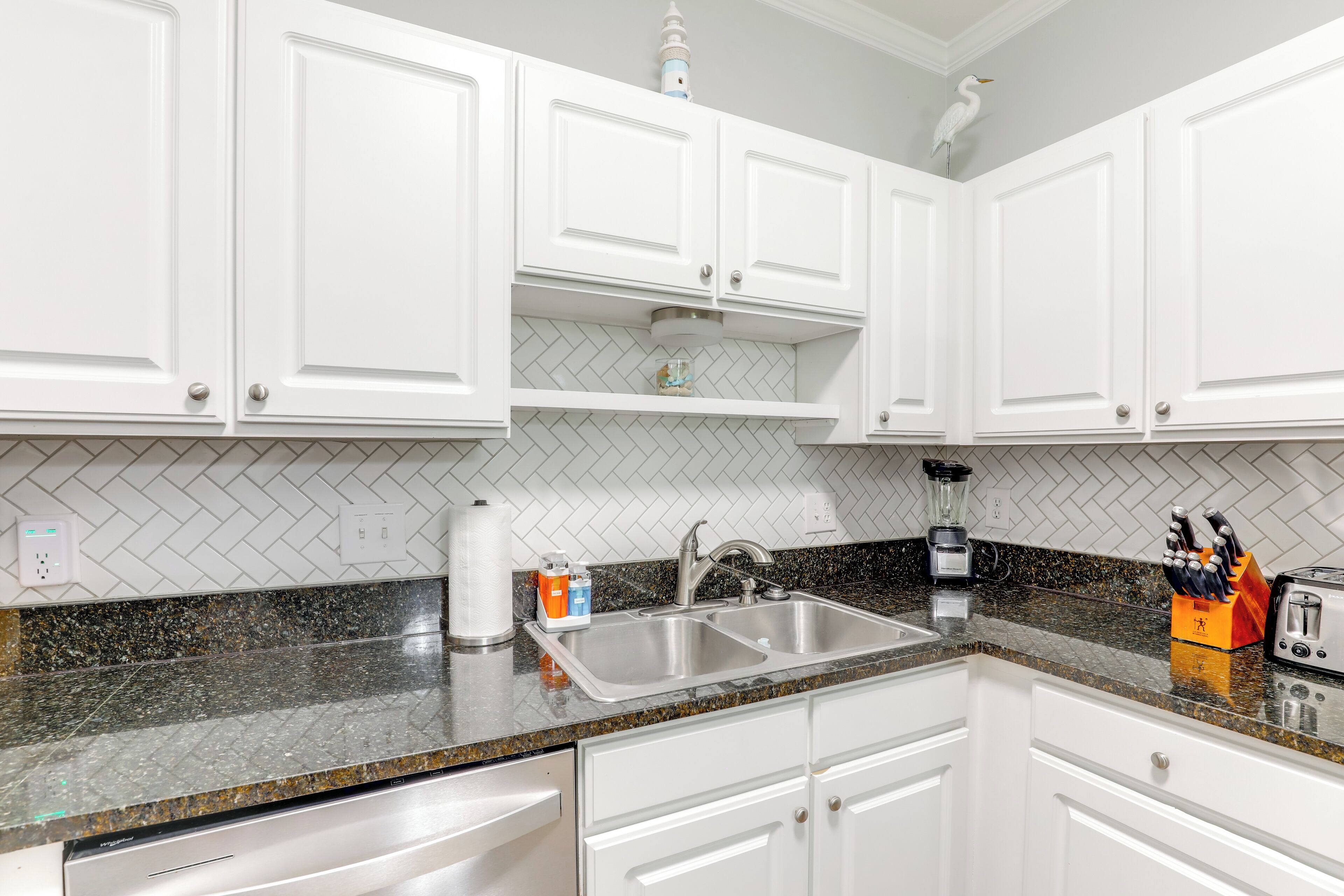 A kitchen with white cabinets, a granite countertop, a double sink, and a toaster.