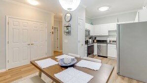 A modern kitchen with white cabinets, a stainless steel refrigerator, and a dining area with a wooden table and white placemats. - < 2 Mi to Beach: Savannah Shores Resort Condo! (Myrtle Beach)