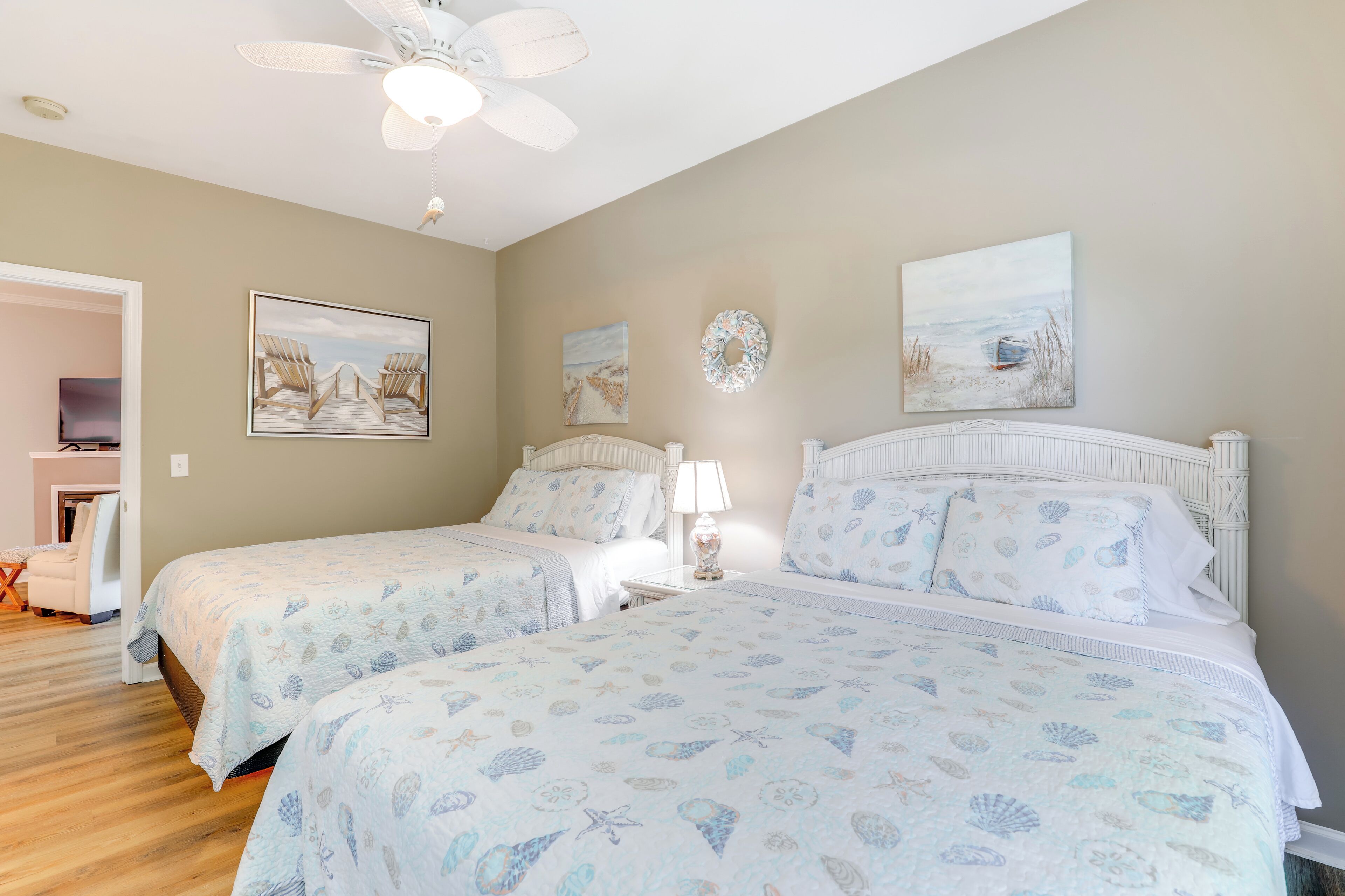 A bedroom with two beds, a ceiling fan, and artwork on the walls.