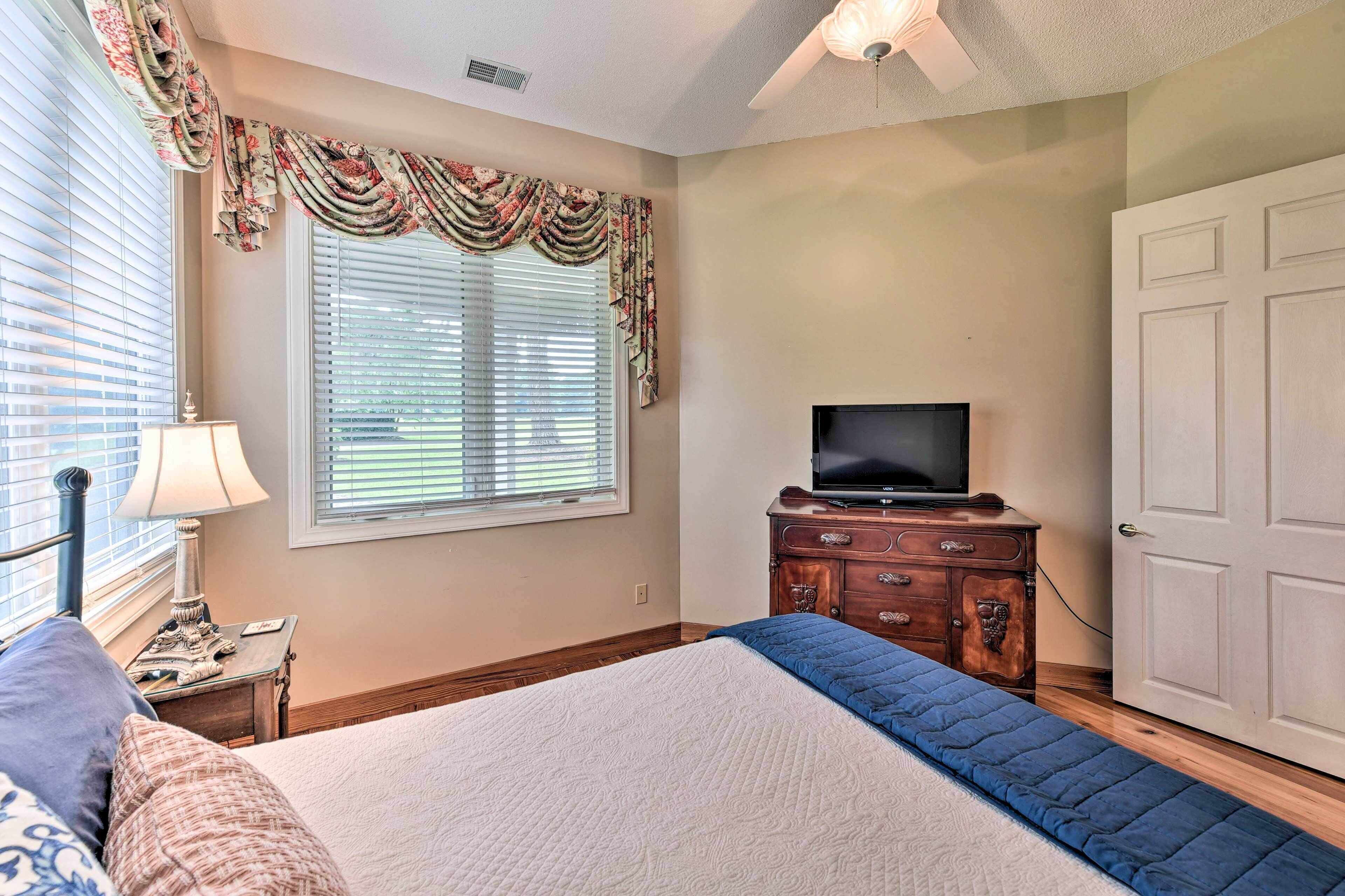 A bedroom with a bed, a dresser, a television, and a window with blinds.