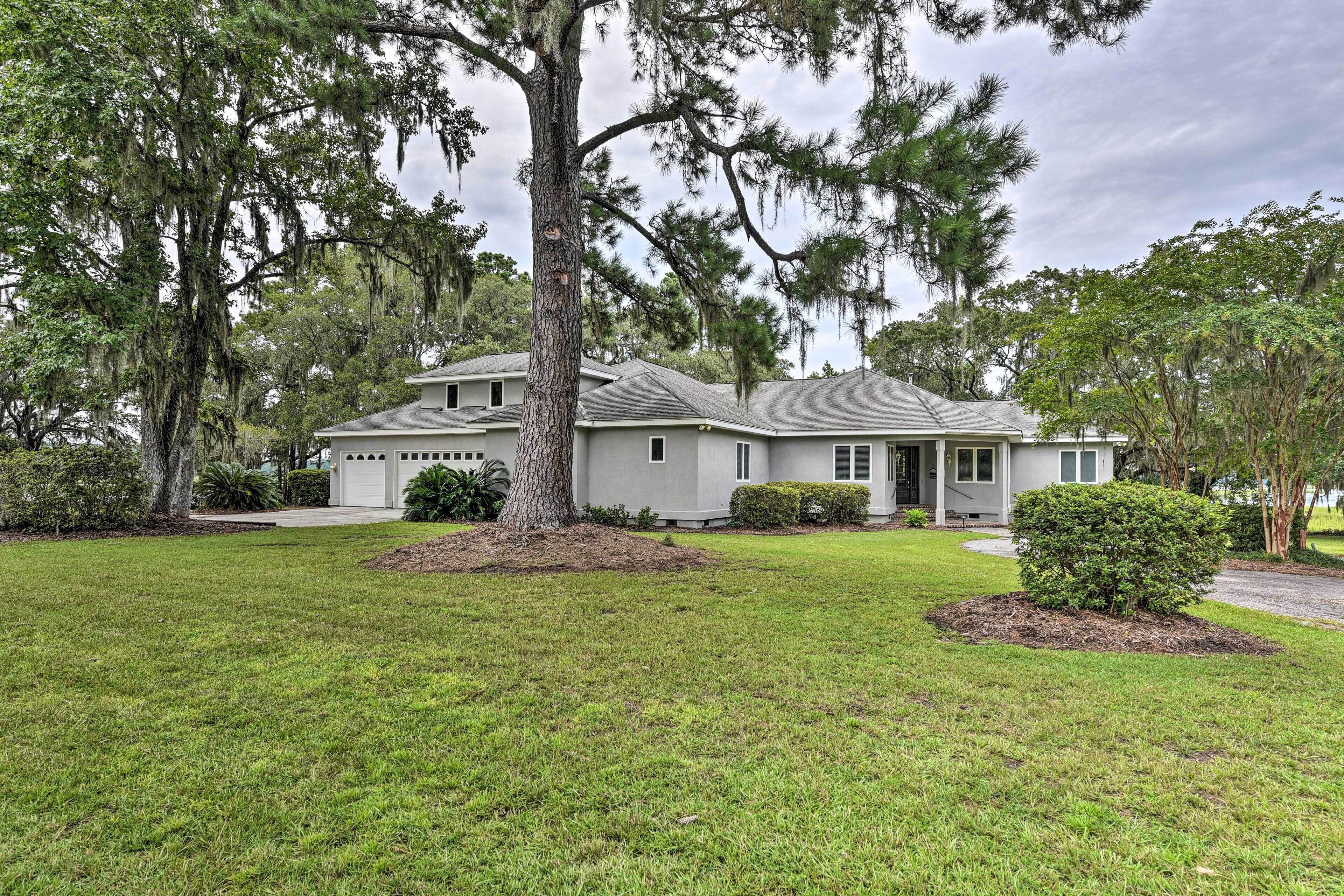 A two-story house with a large front yard, a garage, and mature trees.