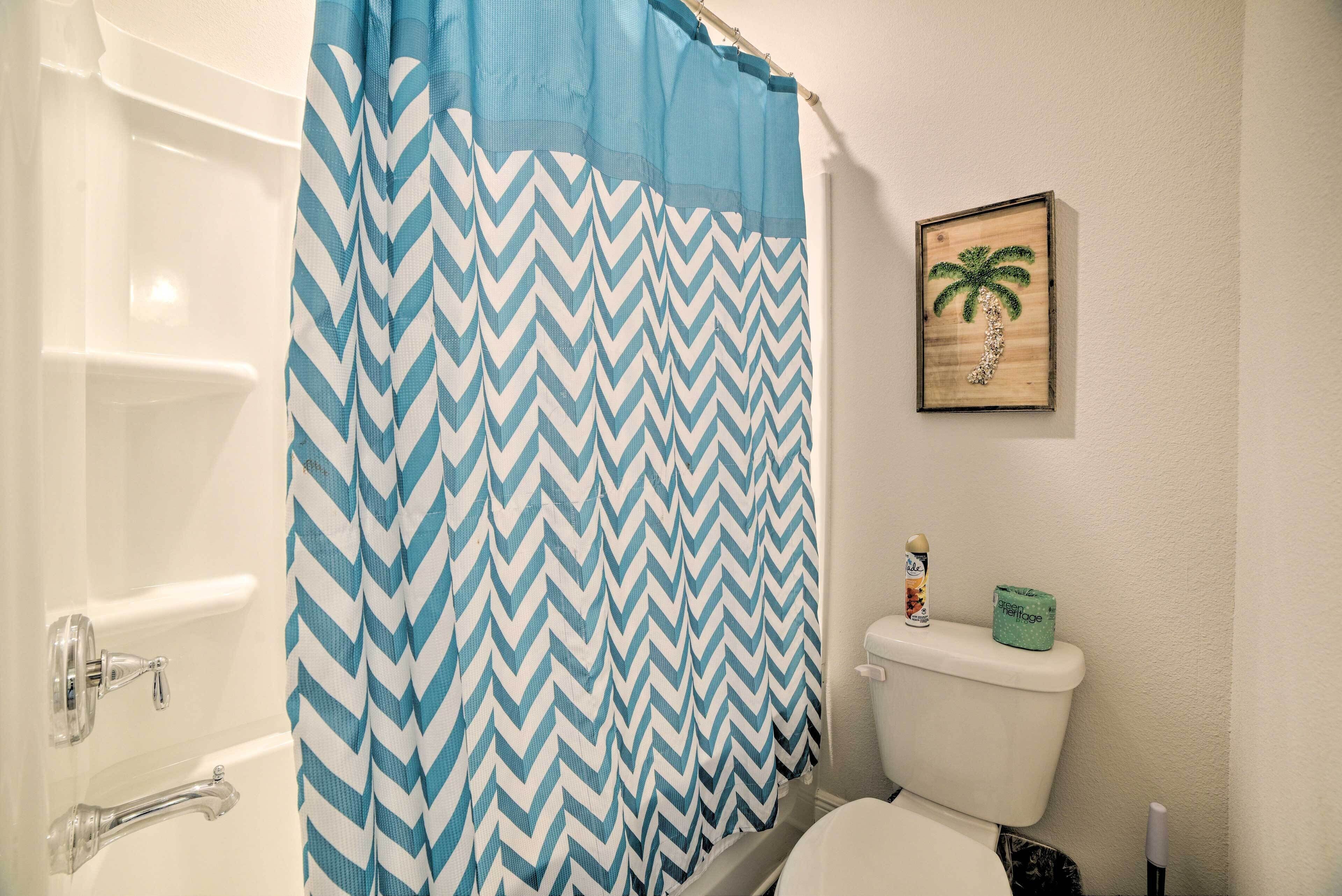 A bathroom with a blue and white chevron shower curtain, a toilet, a framed picture of a palm tree, and a roll of toilet paper on the toilet tank.