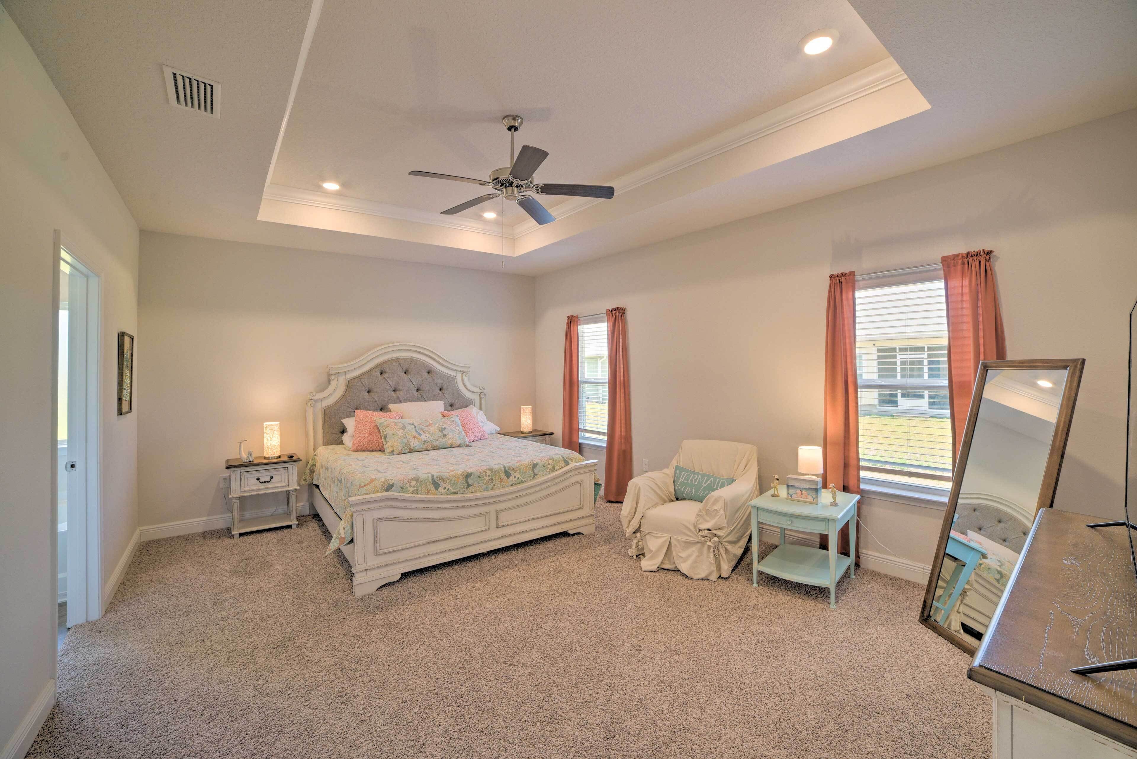 A bedroom with a bed, a chair, a desk, a ceiling fan, and a window with curtains.