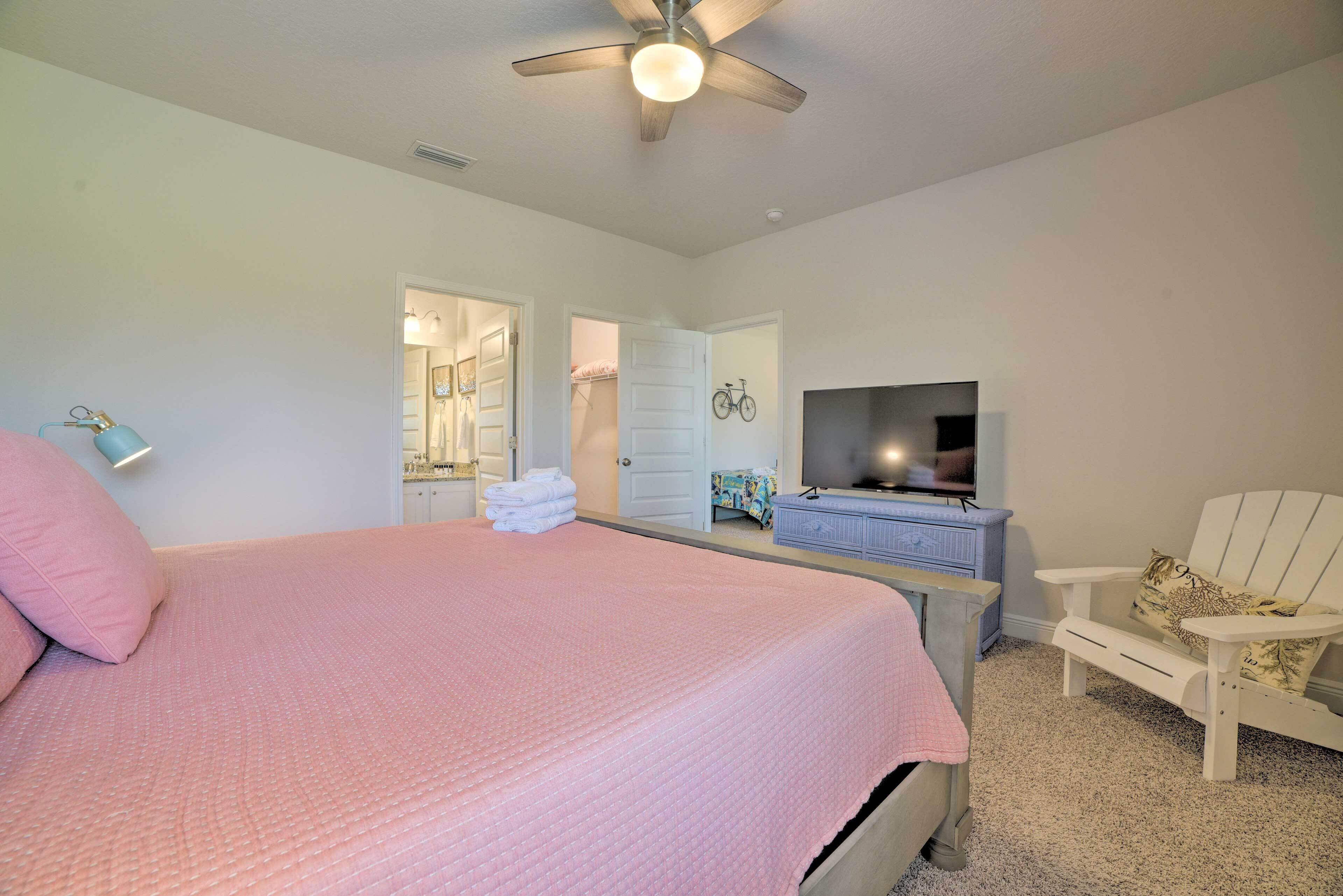 A bedroom with a large bed, a ceiling fan, a dresser, a television, and a chair.