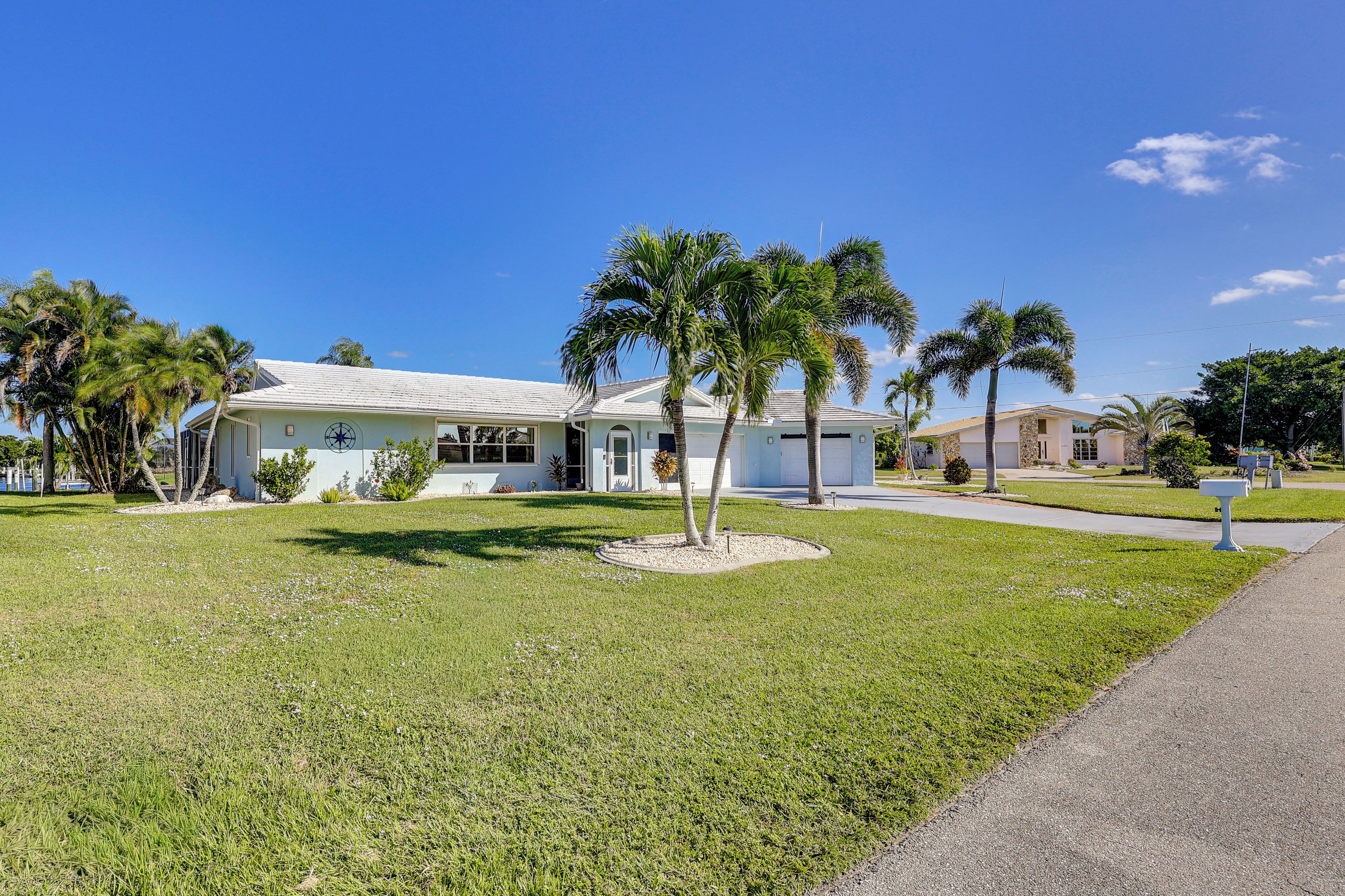 A single-story house with a white exterior, a covered porch, and a well-maintained lawn with palm trees.