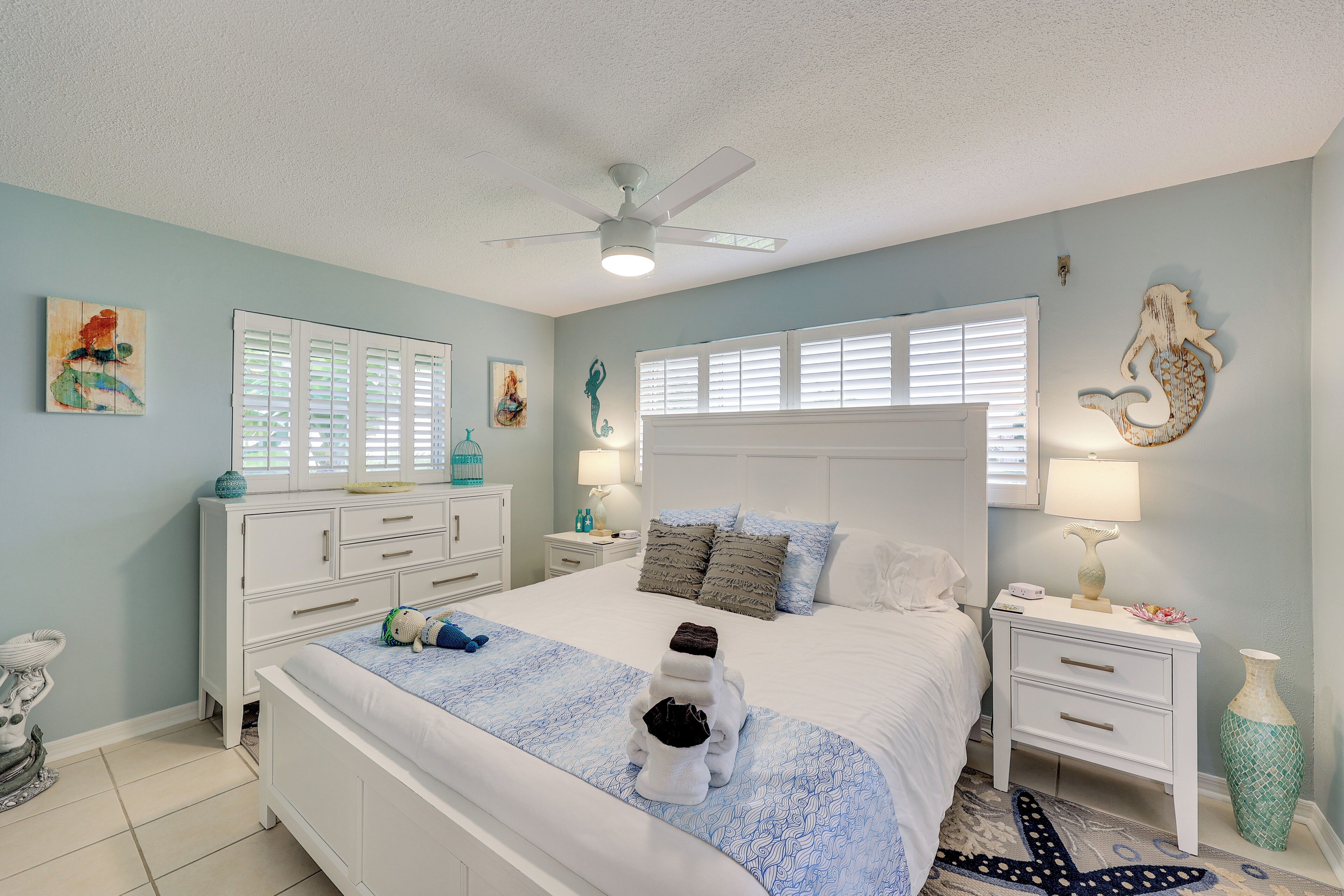 A neatly arranged bedroom with a bed, bedside tables, a nightstand, and a ceiling fan.