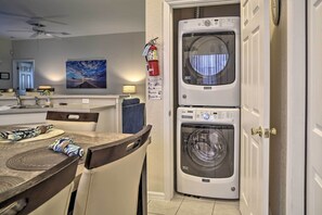 Una sala de bugaderia amb dues rentadores superposades davant, un extintor i un senyal de via d'emergència fixat a la paret.