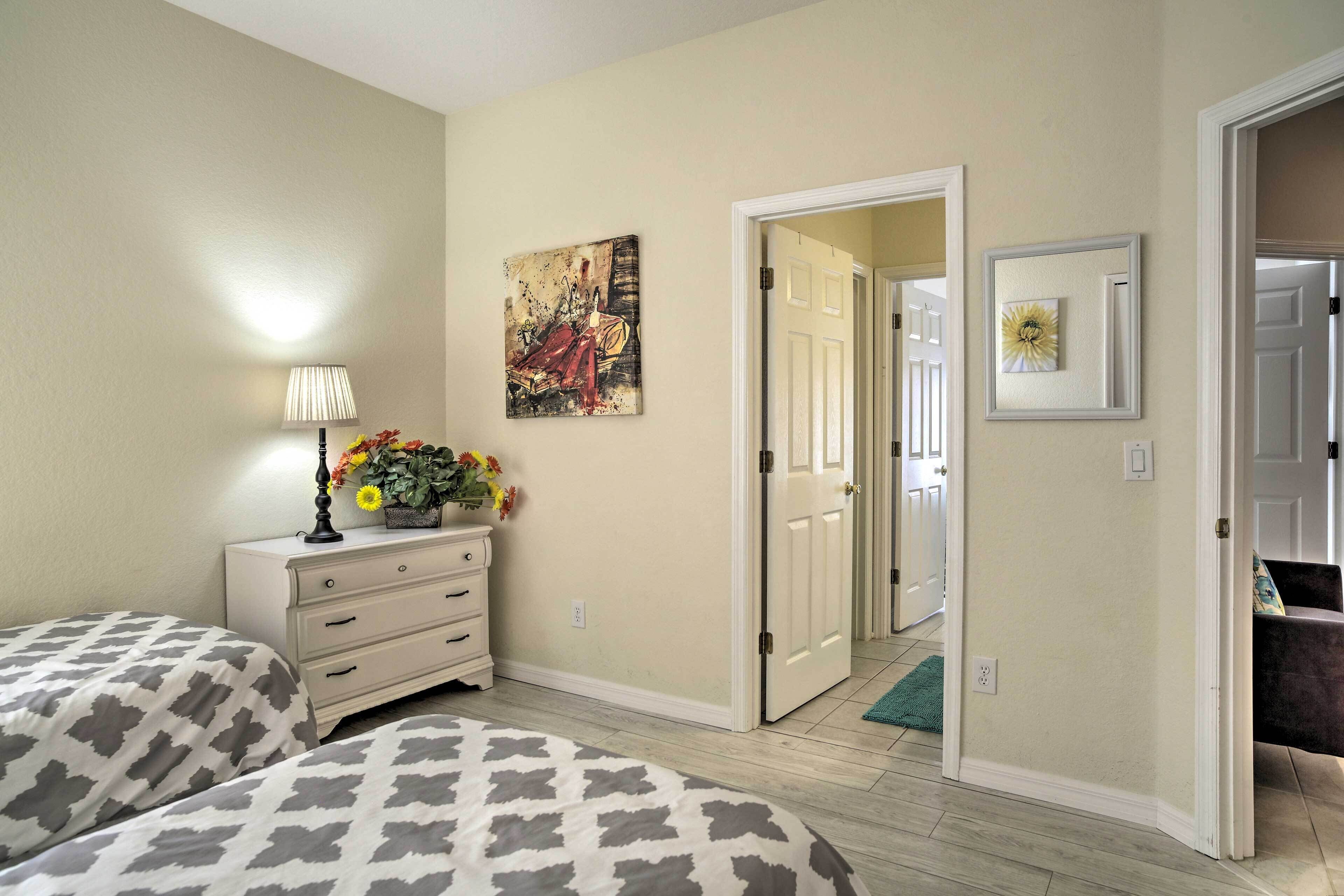 A bedroom with two beds, a dresser, a lamp, and a painting on the wall.