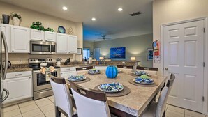 A modern kitchen with white cabinets, stainless steel appliances, and a dining area with a large table set for six. - Spacious Clermont Getaway ~ 10 Miles to Disney! (Clermont)