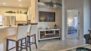 A modern kitchen with a built-in refrigerator, white cabinets, and a large flat-screen TV. There is a dining area with bar stools and a small table. - Spacious Clermont Getaway ~ 10 Miles to Disney! (Clermont)