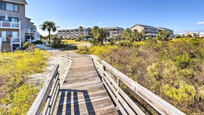 A wooden boardwalk leading to a beachfront property with multiple-story buildings, some with balconies and a pool area. - St Helena Island Condo w/ Pool & Beach Access! (Harbor Island)
