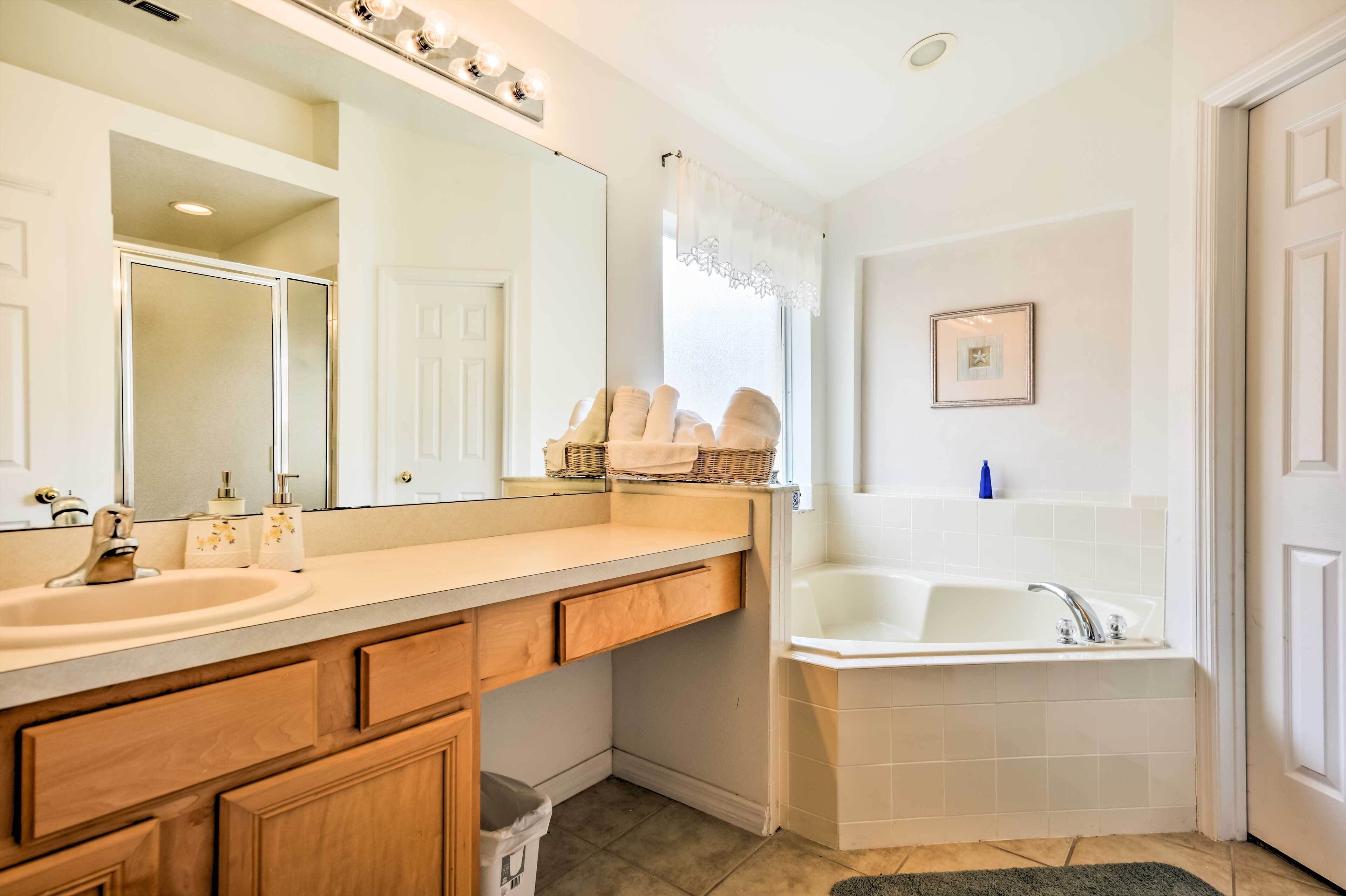 A bathroom with a large mirror, two sinks, a bathtub, and wooden cabinets.
