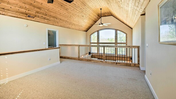 Una habitació àmplia amb sostre inclinat, una finestra gran i un balcó amb barana.