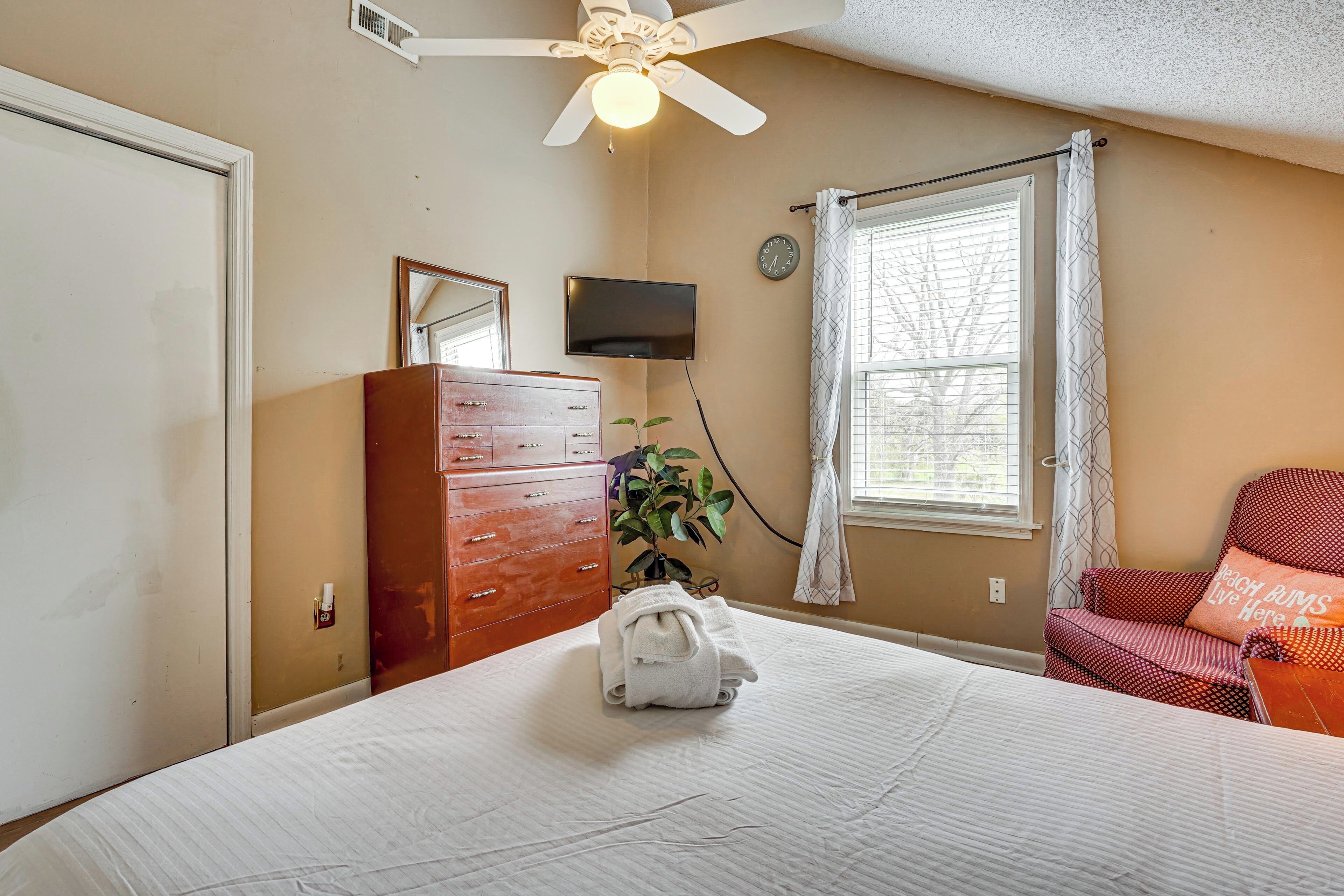 Quarto com cama, cômoda, televisão, relógio e janela com cortinas.