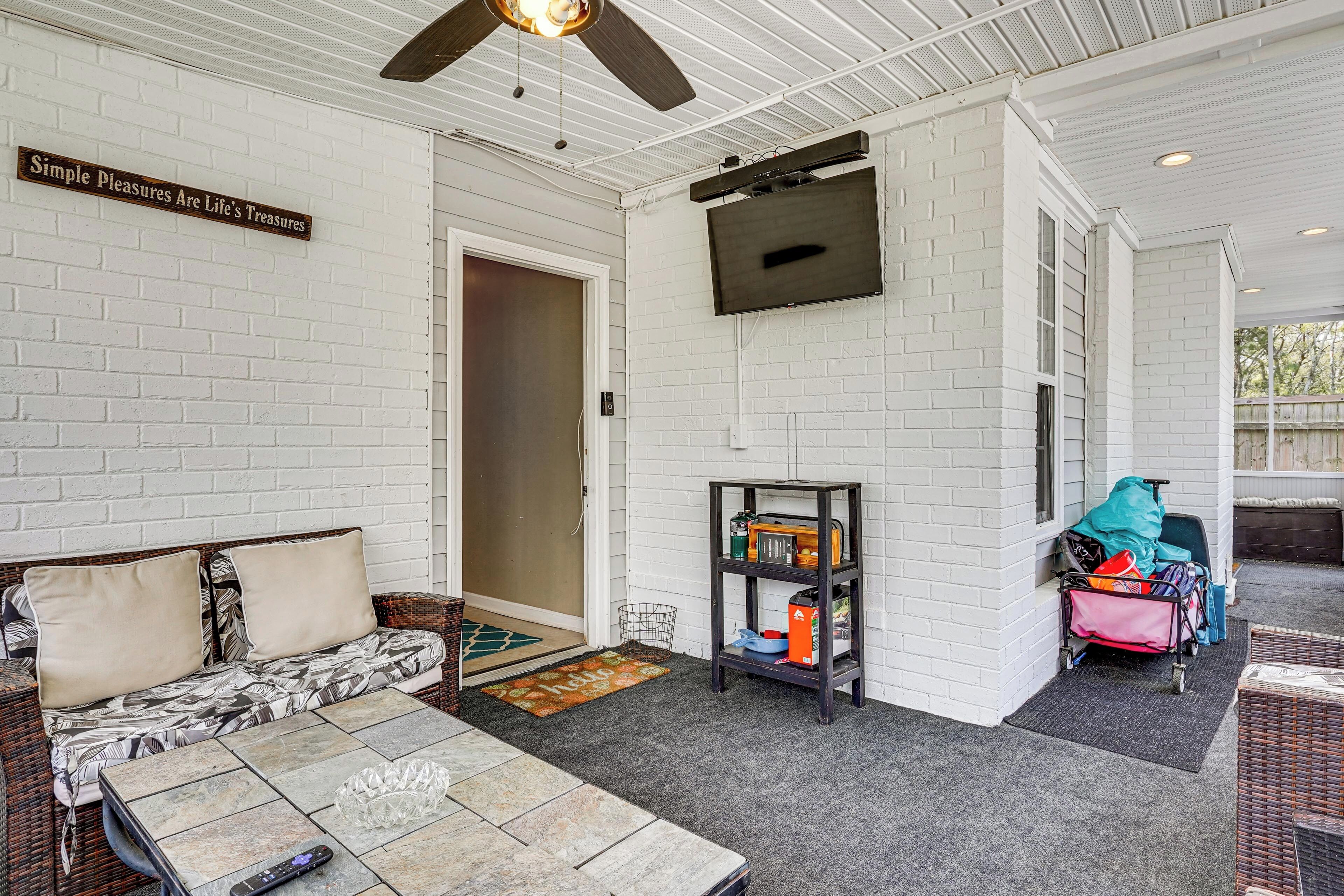 A covered patio with a sofa, a television mounted on the wall, and a luggage cart.