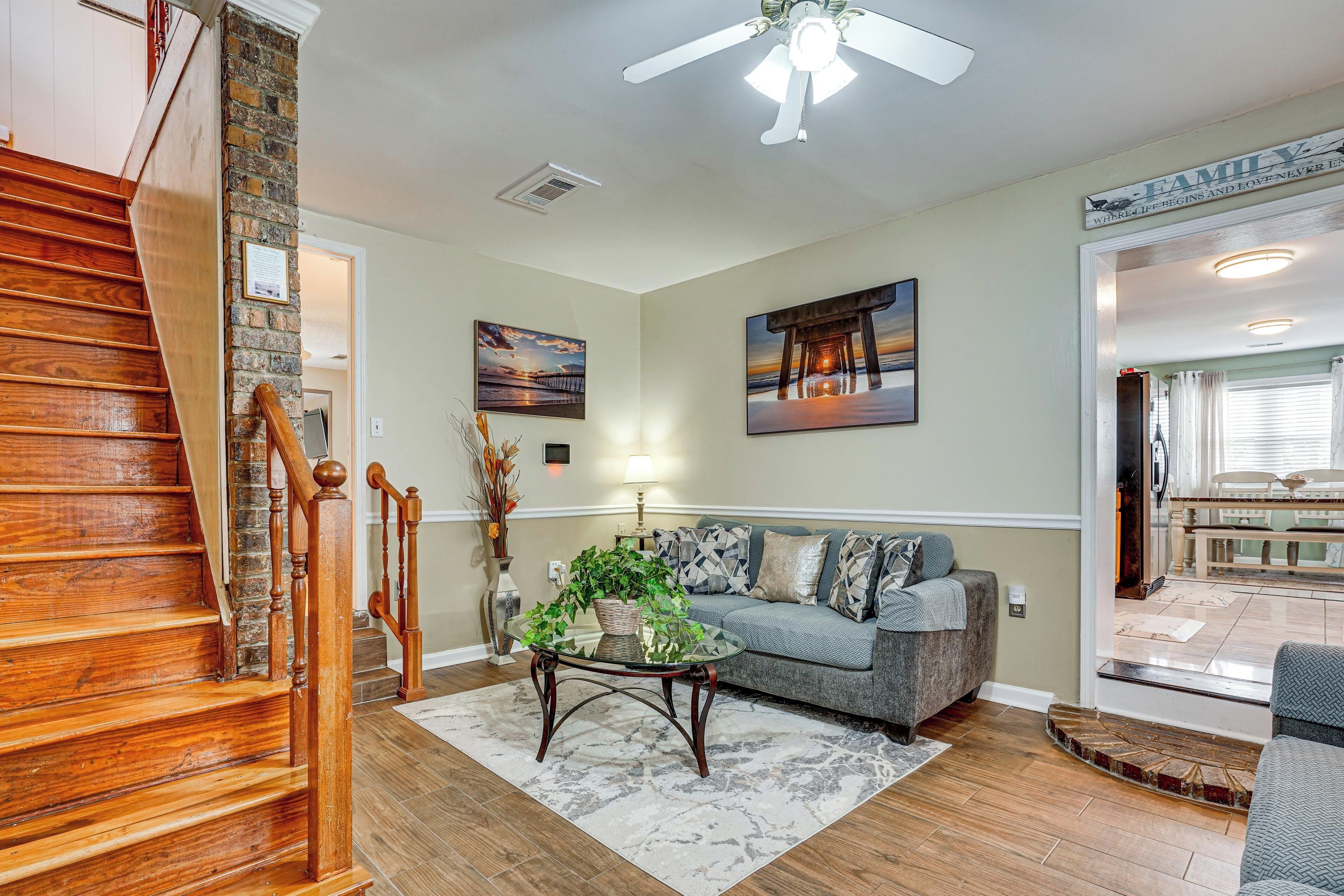 A living room with a wooden staircase, a glass coffee table, a grey sofa, and a ceiling fan.