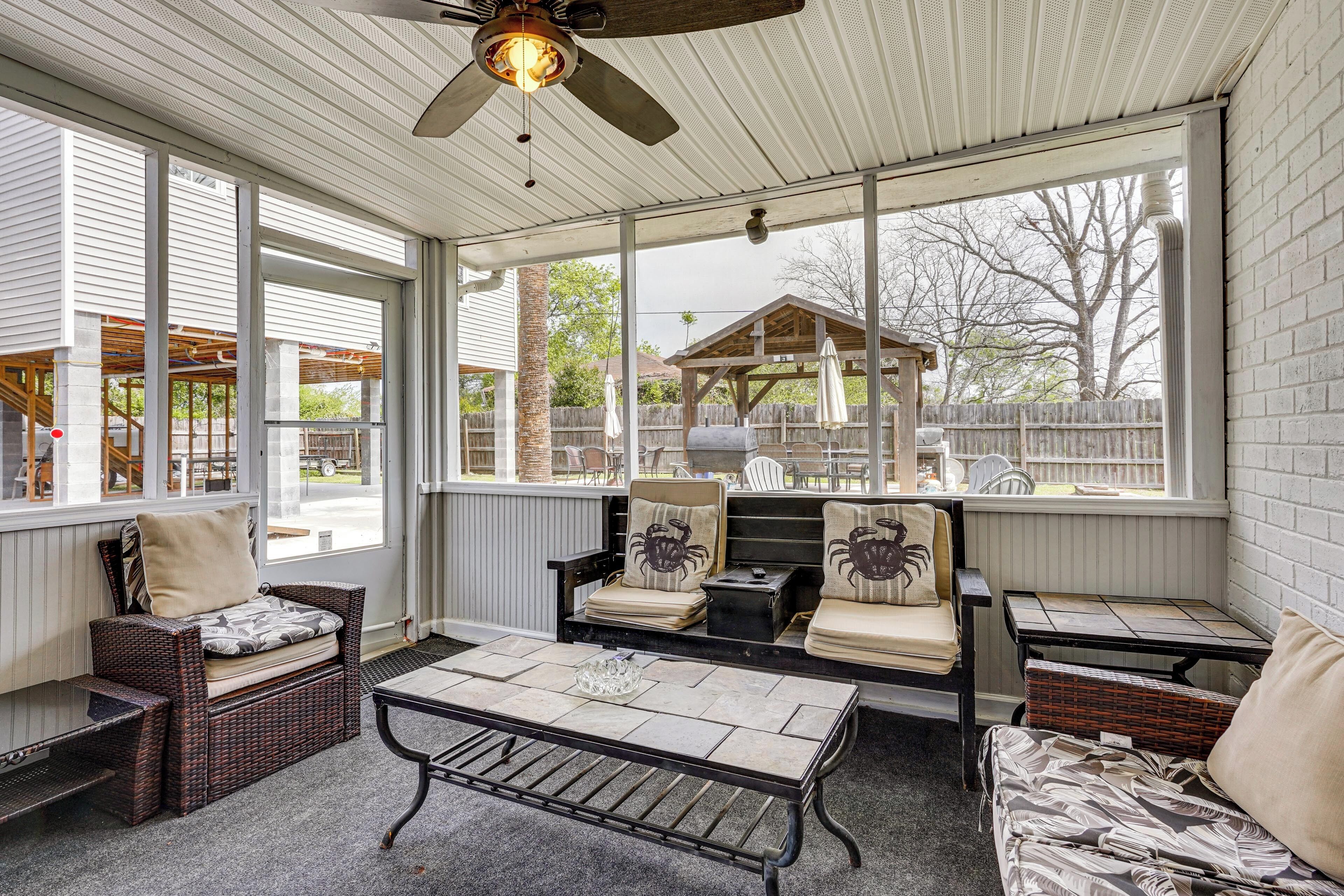 A covered patio with wicker furniture, a table, and a ceiling fan.