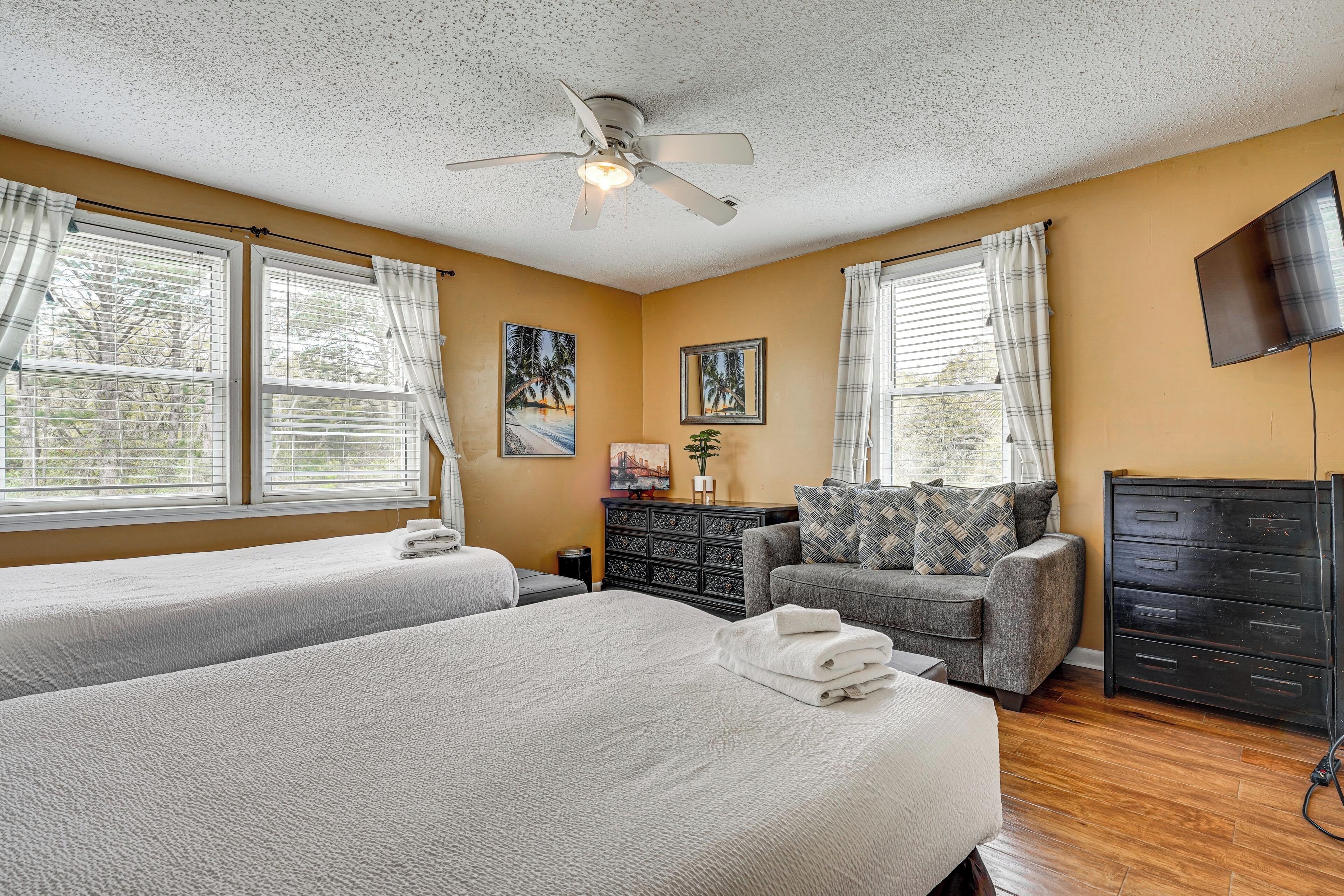 A hotel room with two beds, a ceiling fan, a TV, a sofa, and a dresser.