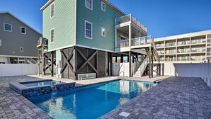 Une piscine avec une terrasse en briques, un bâtiment écologique doté d’un balcon, et un bâtiment blanc en arrière-plan.