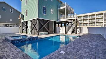 Piscina com deck de tijolos, um edifício verde com varanda e um edifício branco ao fundo.