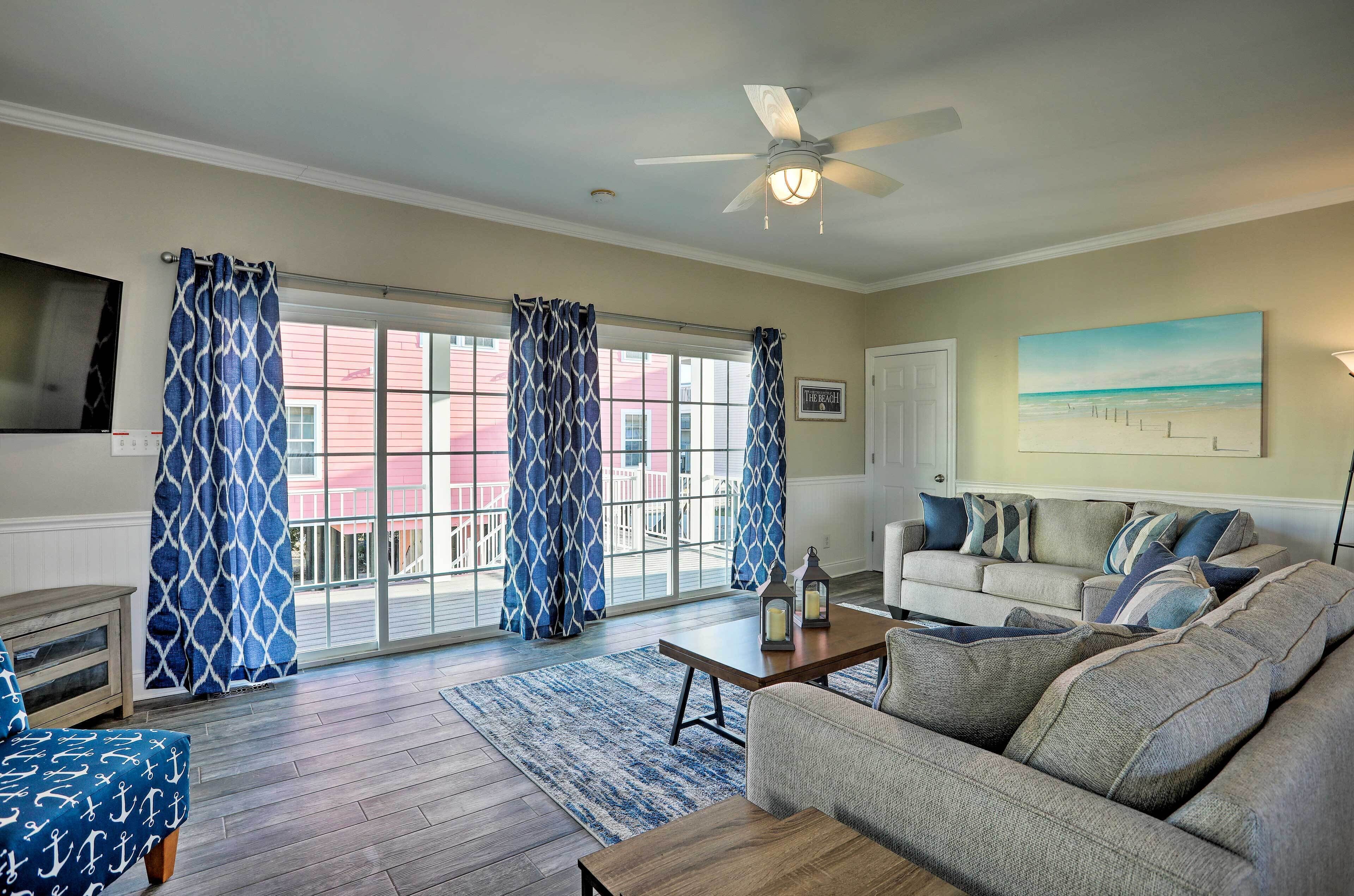 A living room with a sofa, a coffee table, and a TV. There are curtains on the windows, and a painting on the wall.
