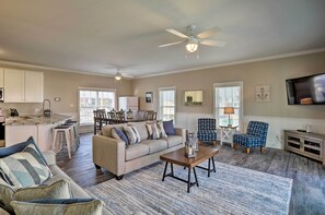 A spacious living room with a sofa, coffee table, and a TV. There is a dining area with a table and chairs, and a kitchen with cabinets and a refrigerator. - Spacious Murrells Inlet Hub w/ Pool, Walk to Shore (Murrells Inlet)
