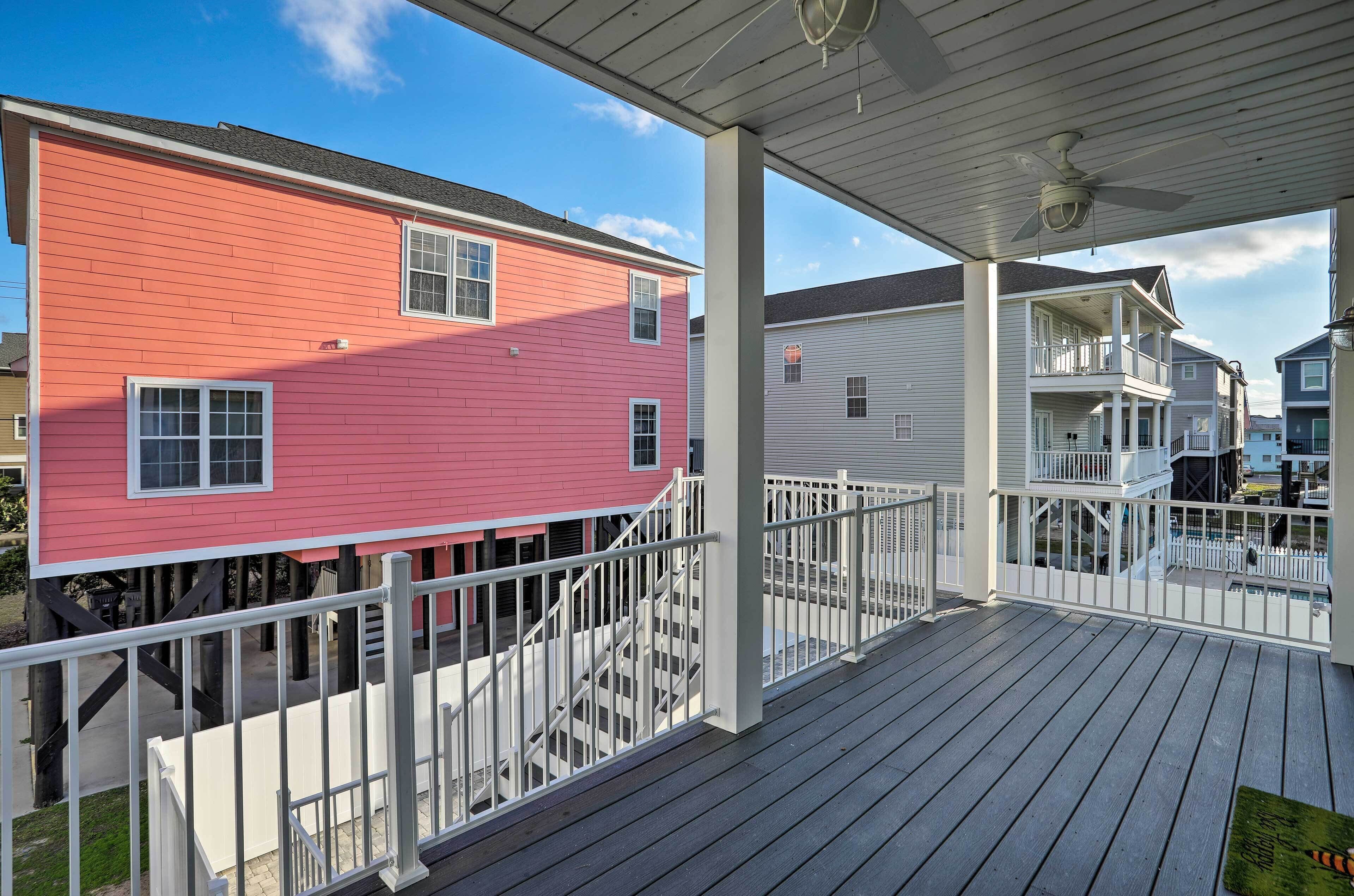 A residential deck with a white railing, a ceiling fan, and a view of neighboring houses.