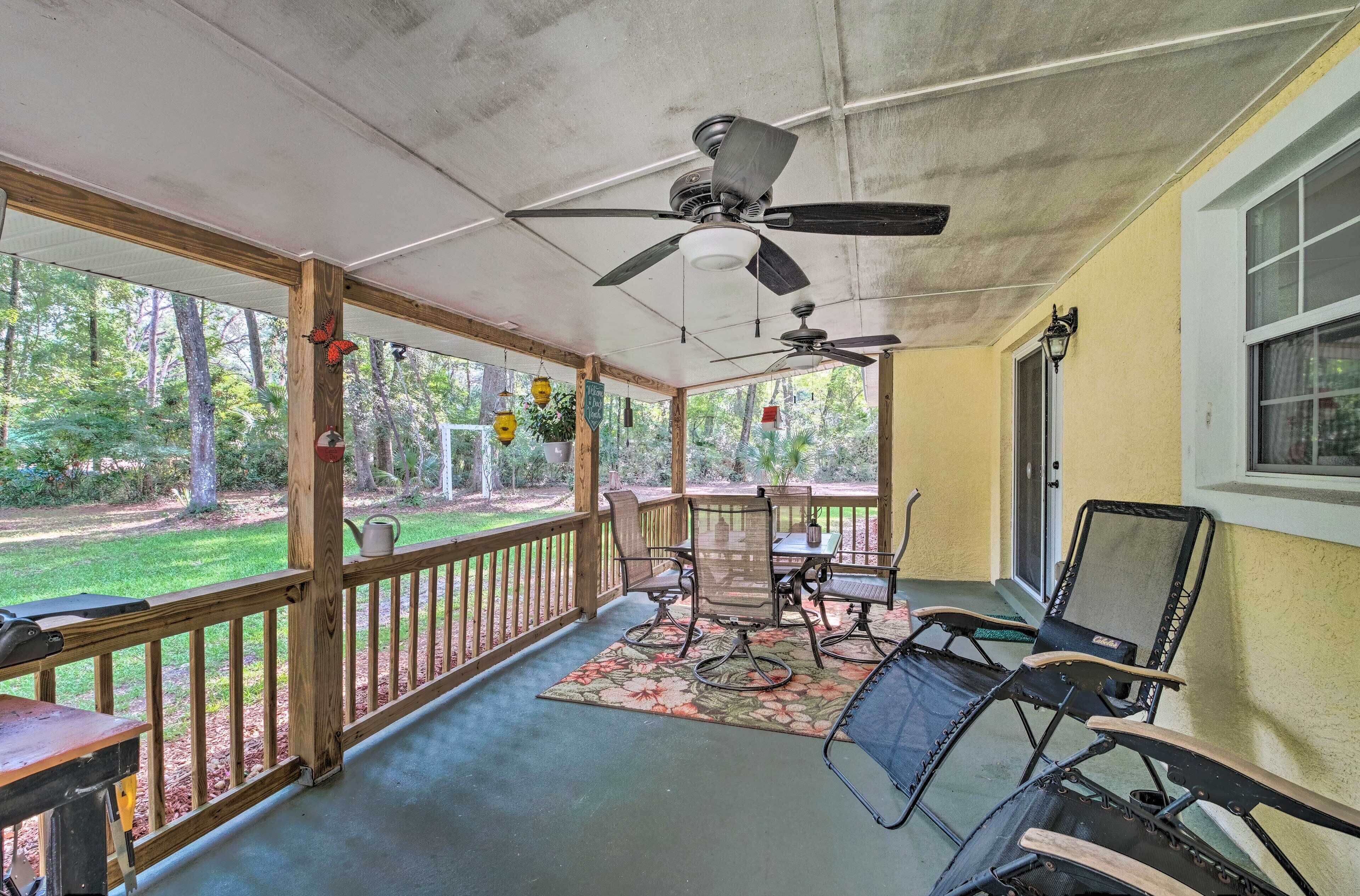 A covered porch with a table and chairs, a ceiling fan, and a view of the surrounding forest.