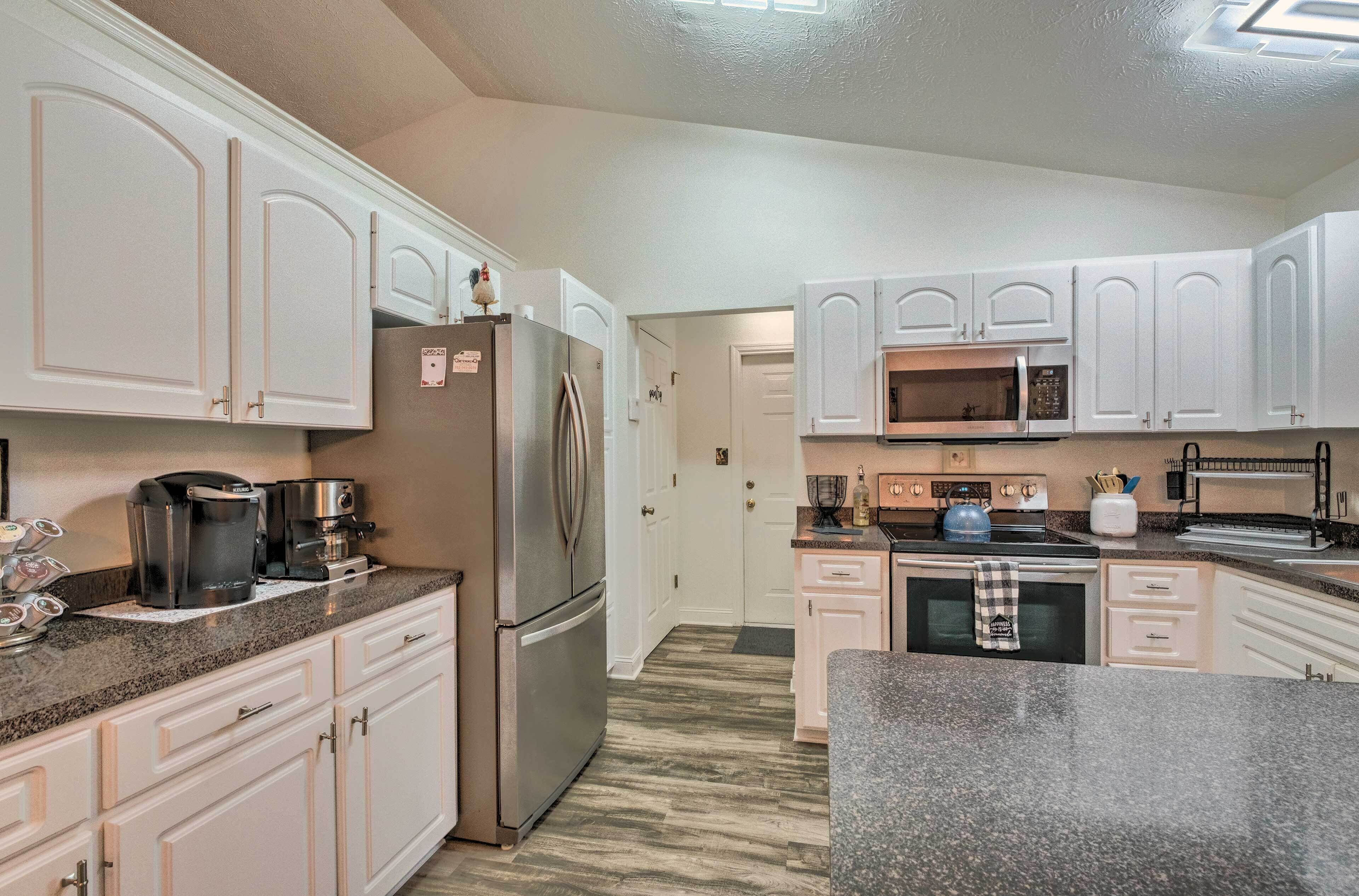 Een keuken met witte kastjes, roestvrijstalen apparatuur, granieten aanrecht en een magnetron.