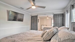 Un dormitorio con cama, ventilador de techo, televisor montado en la pared y puerta corrediza.