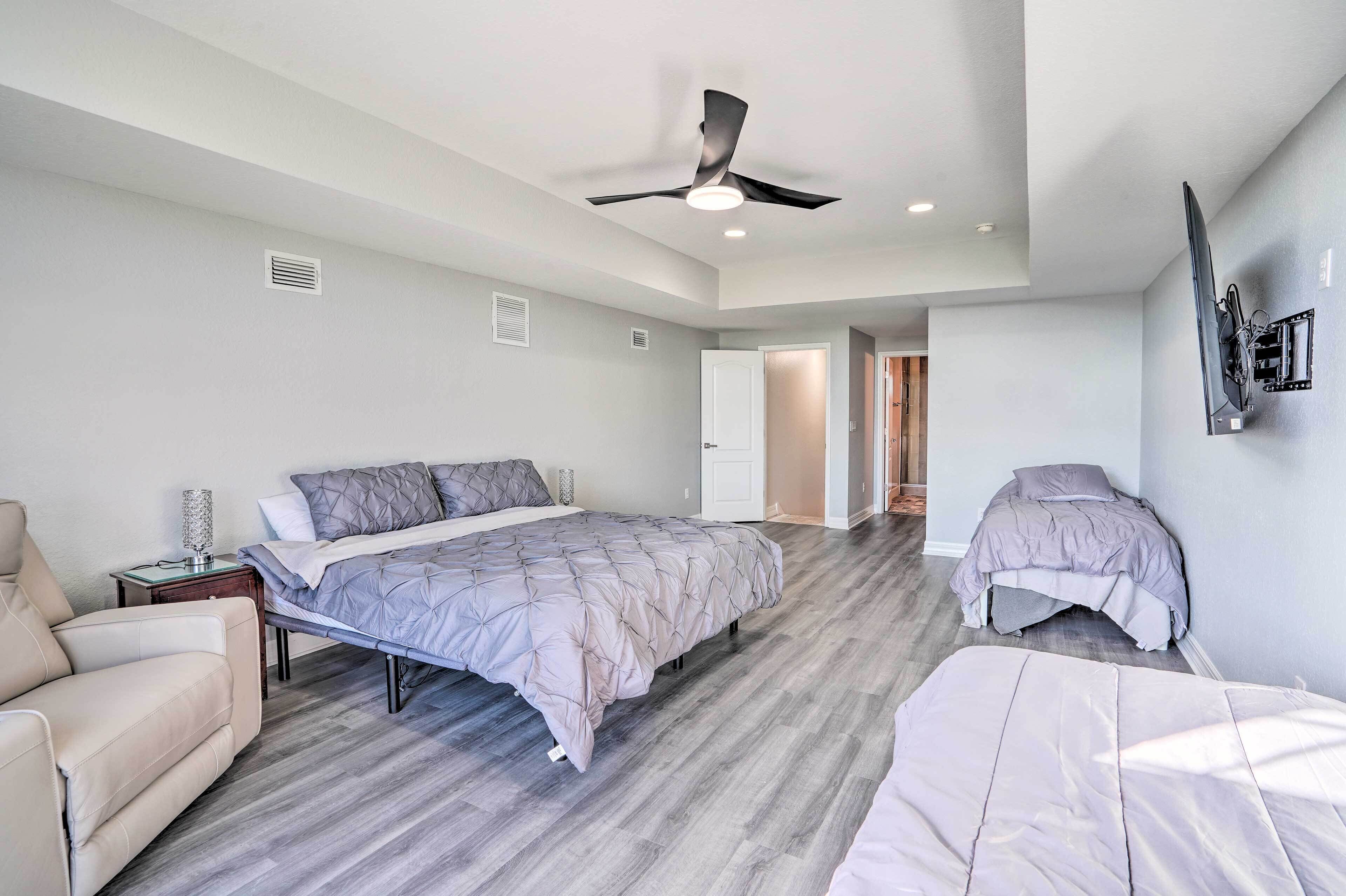 Une chambre avec un grand lit, un lit plus petit, un canapé, un ventilateur de plafond et un téléviseur fixé au mur.