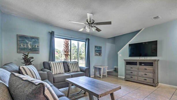 A living room with a sofa set, a coffee table, a TV, and a ceiling fan. - Stylish Bayfront Townhome < 10 Mi to Beach! (Mary Esther)