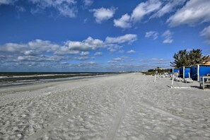 Una playa con cielo despejado, huellas en la arena y un edificio con toldos azules.