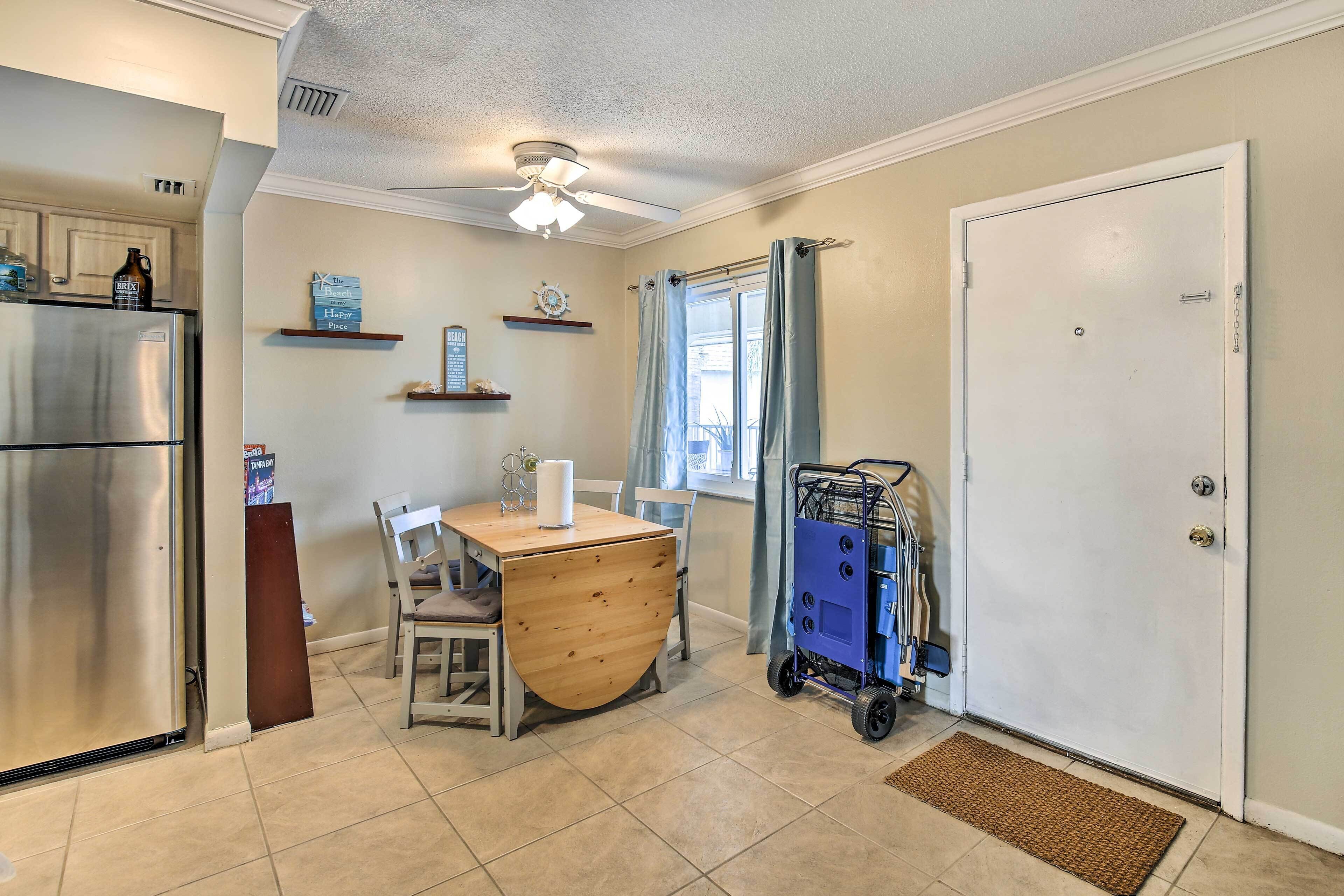 A kitchen with a refrigerator, a wooden table, chairs, a ceiling fan, and a blue cart near a door.