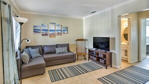 A living room with a sofa, a TV, a lamp, and a bookshelf. - Walk to Beach & Dining: Sunny St Pete Condo! (St. Pete Beach)