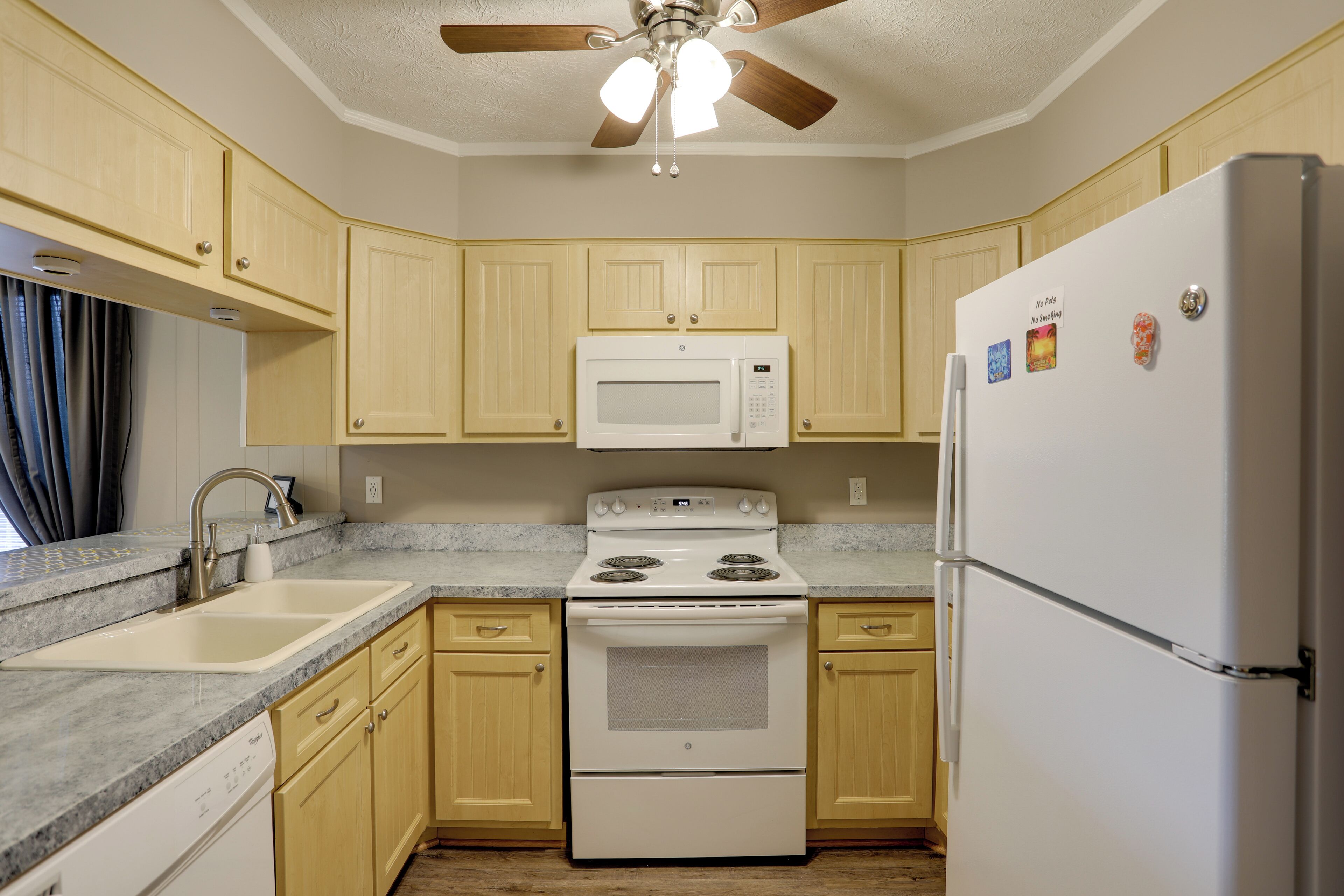 Una cocina con gabinetes de madera, una estufa blanca, un microondas y un refrigerador.