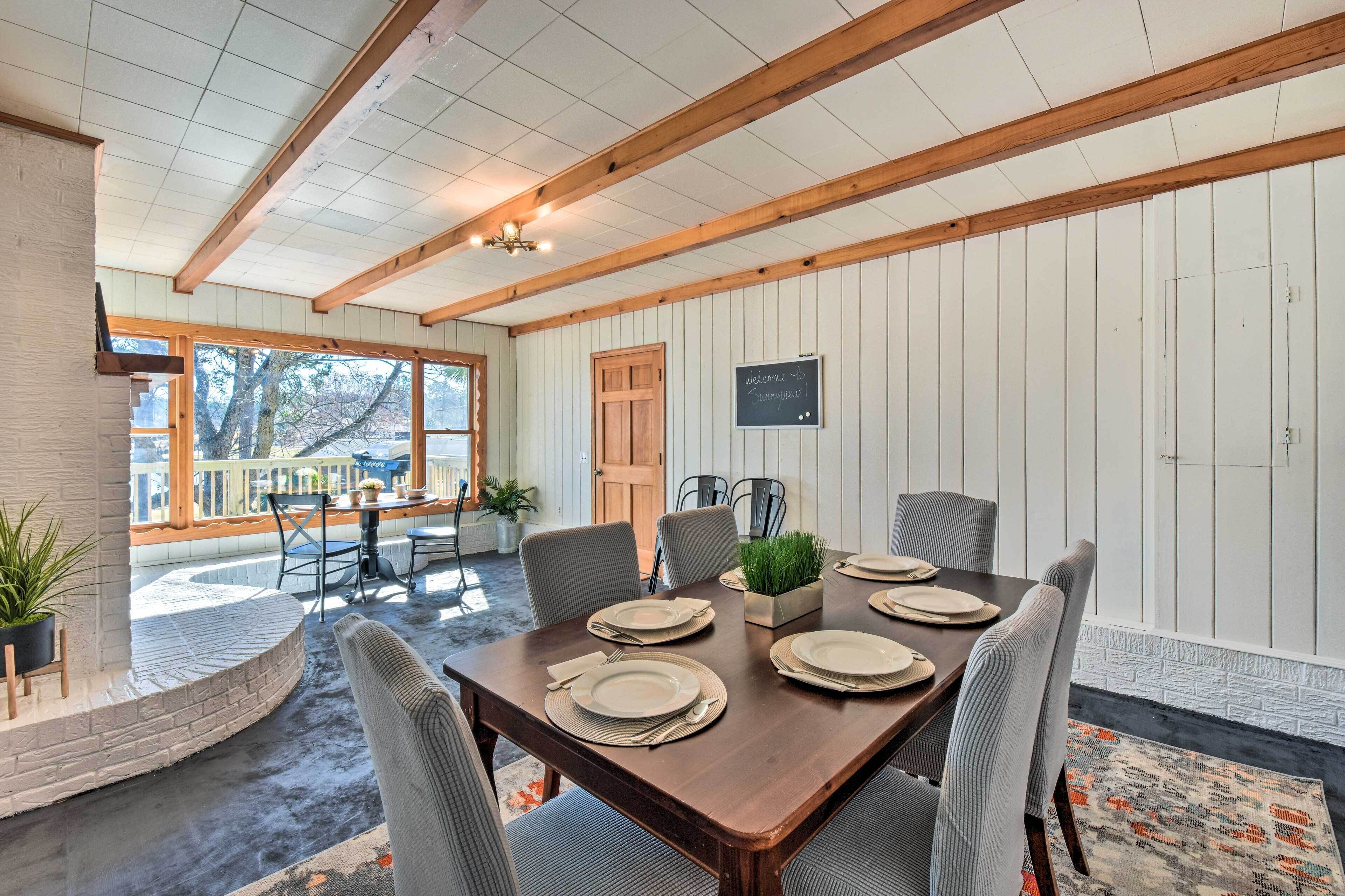 Un coin repas avec une table en bois dressée pour quatre personnes, entourée de chaises. Un panneau noir affiche l’inscription : « Bienvenue chez [nom] ».