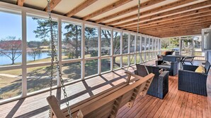 Een overdekt terras buiten, met houten balken, grote ramen, rieten meubels en een schommel.