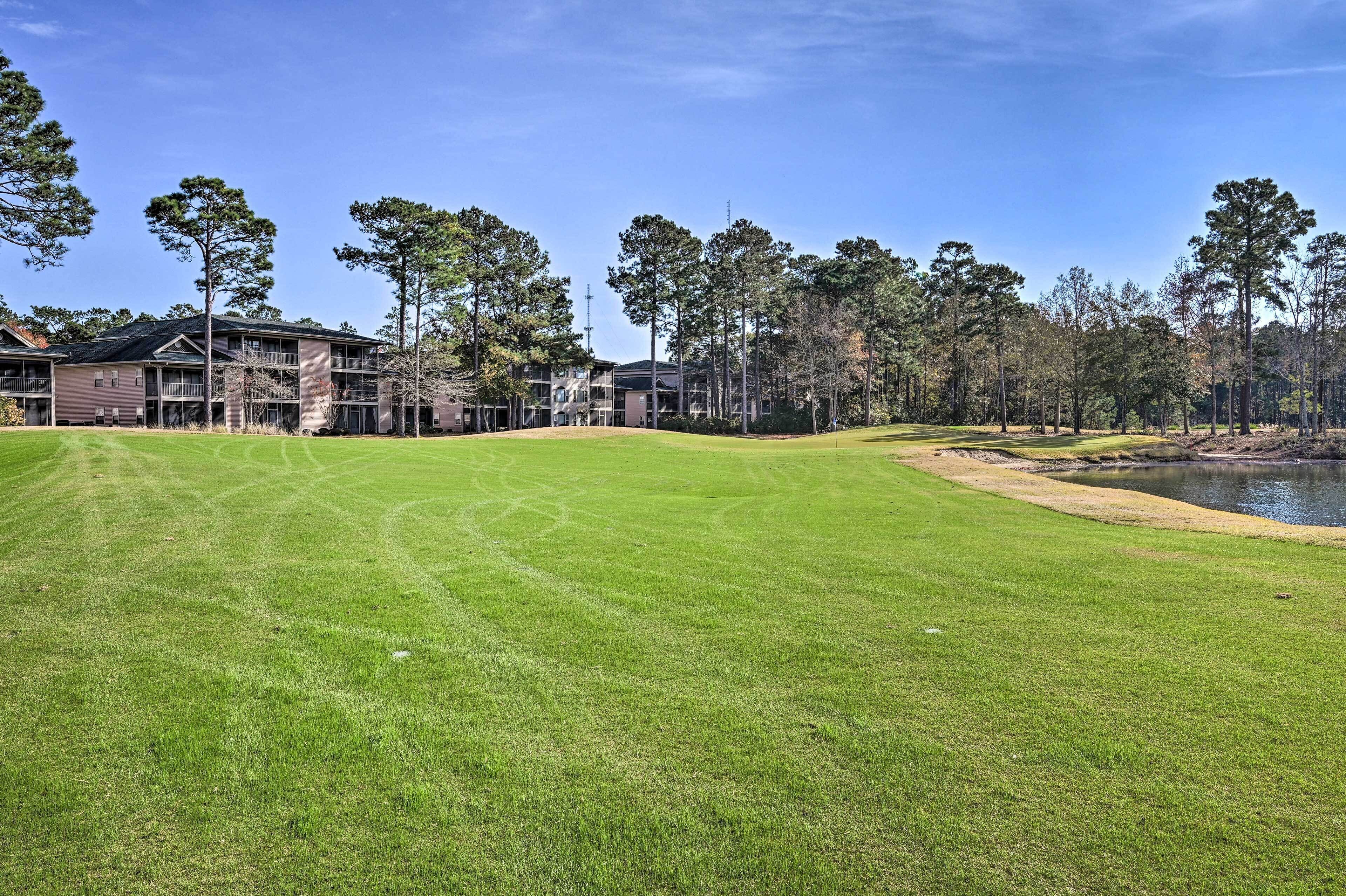 A golf course with a pond, surrounded by trees and buildings.