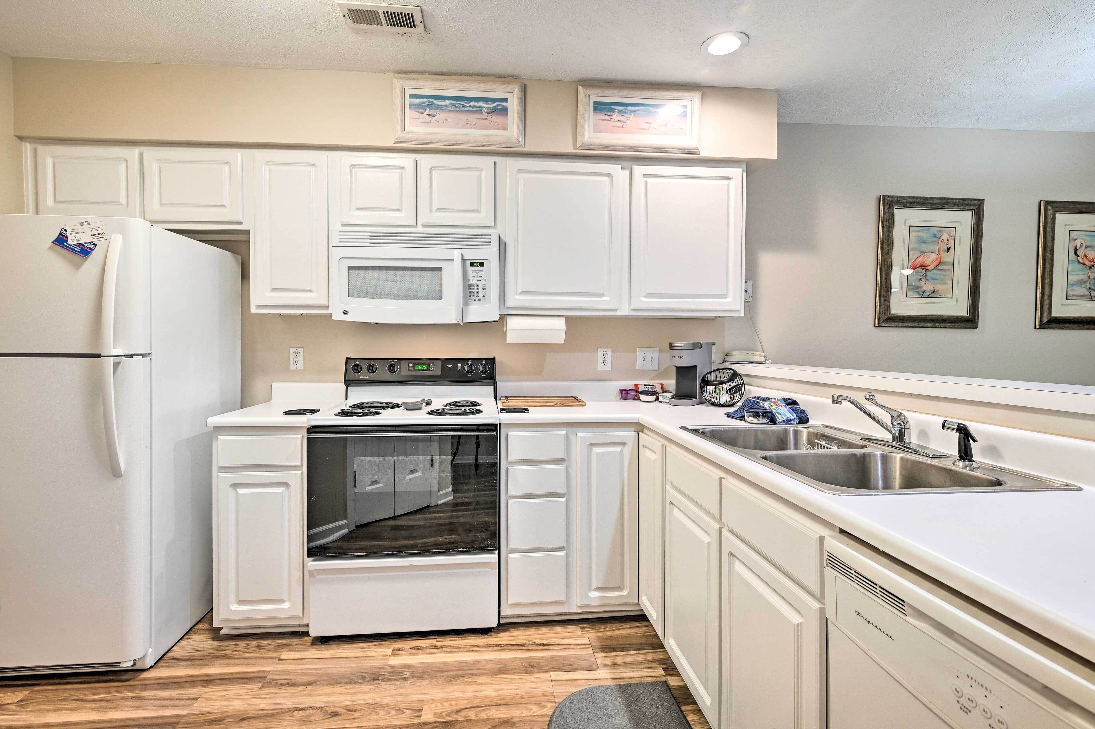 A kitchen with white cabinets, a microwave, a stove, a refrigerator, and a sink.
