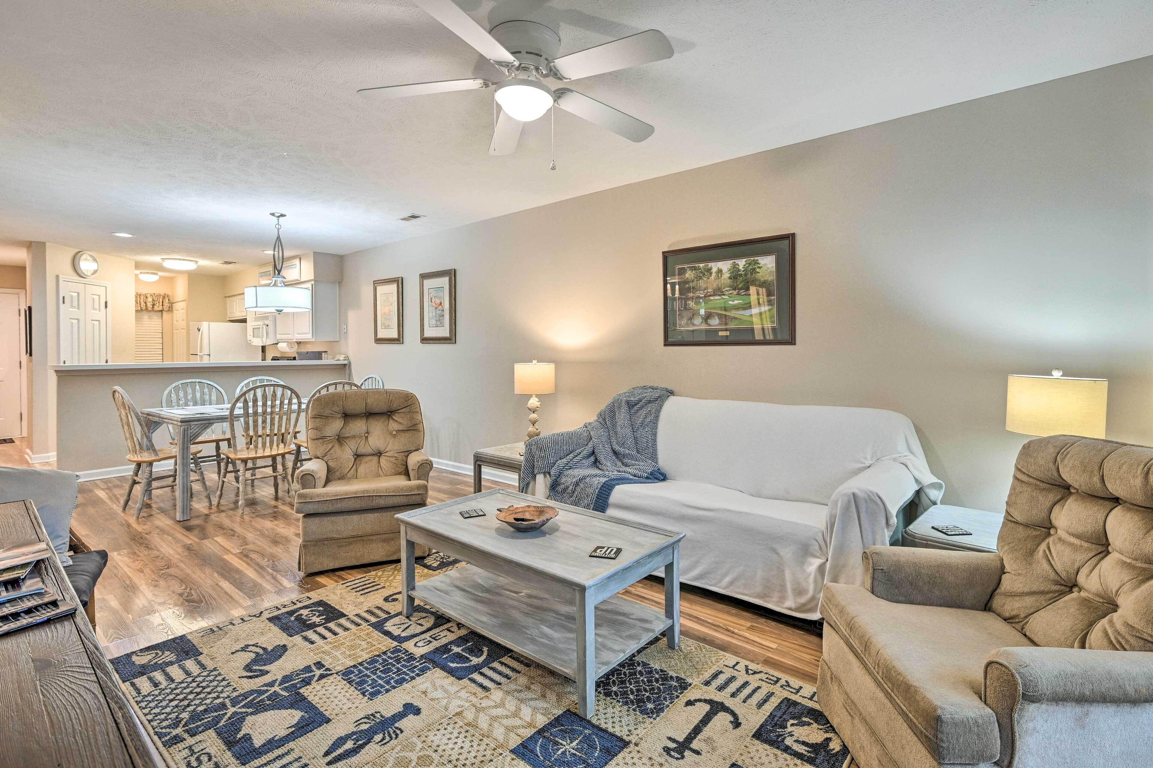 A living room with a sofa, armchairs, a coffee table, and a dining area with chairs and a table.