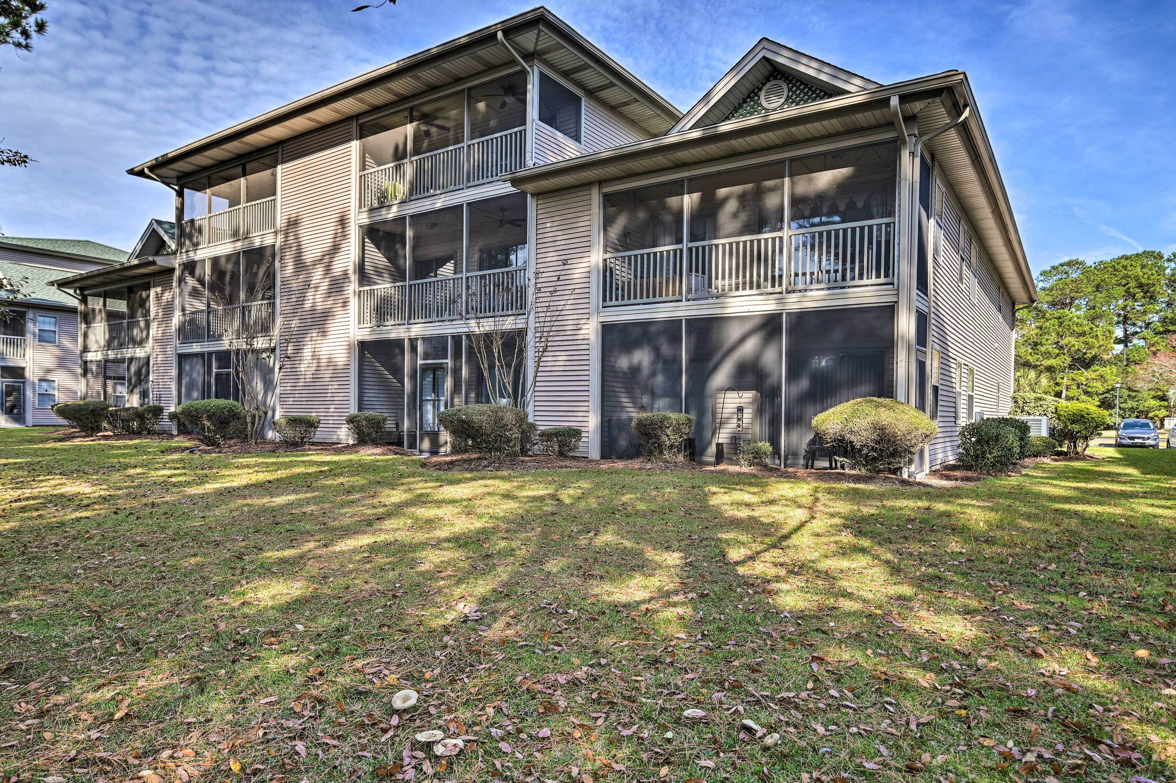 A two-story building with a balcony on the second floor, a covered front porch, and a well-maintained lawn with scattered leaves.