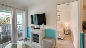 A room with a fireplace, a television mounted above it, a bed with a nightstand, and a glass table with chairs outside. - Across the Street From Ocean: Surfside Beach Condo (Surfside Beach)