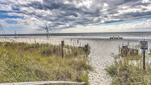 A beach with a wooden walkway leading to the water, a sign warning to keep off dunes, and a structure in the distance. - Across the Street From Ocean: Surfside Beach Condo (Surfside Beach)
